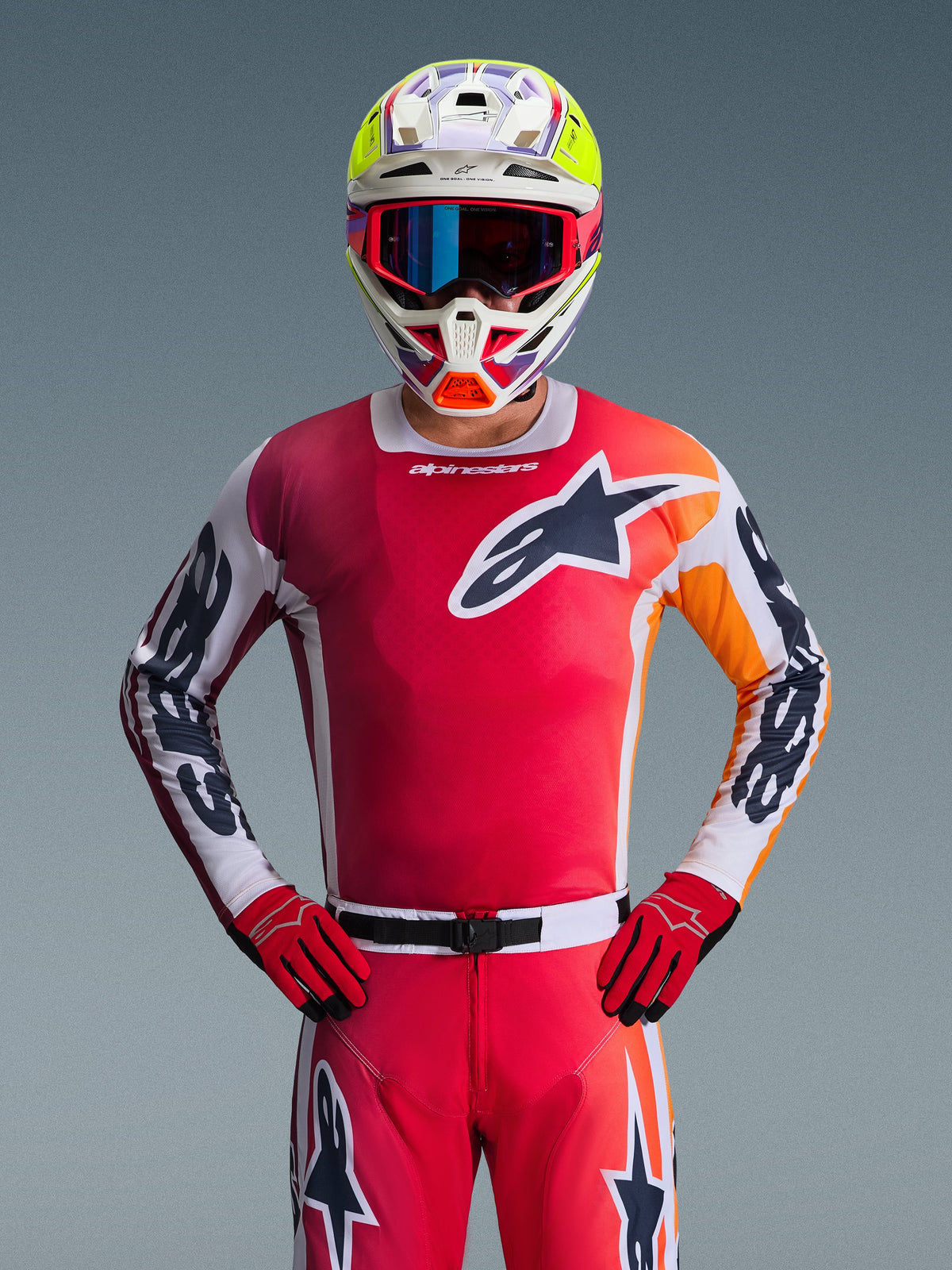 Alpinestars 2026 Racer Portl Gear Set, Motocross-Fahrer in einem leuchtend roten Jersey mit orangefarbenen und weißen Akzenten, passender roter Hose und Handschuhen, mehrfarbigem Helm mit neongelben Highlights und blauer Brille, großes Stern-Logo auf der Brust, professionelle Offroad-Rennausrüstung