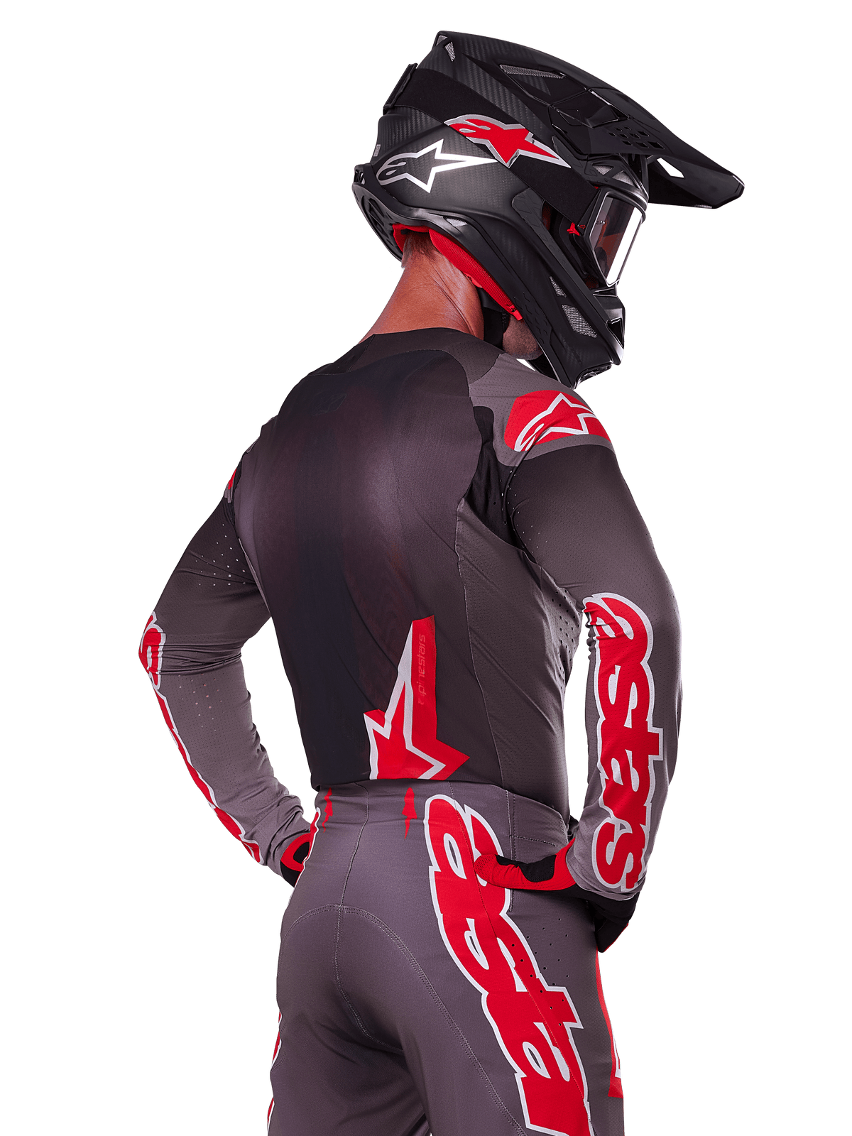 Alpinestars 2025 Supertech Lipan Gear Set, motorcrosser van achteren gezien, antracietgrijze jersey en broek met opvallende rode 'astars' branding op de mouwen en rug, gecombineerd met een zwarte helm