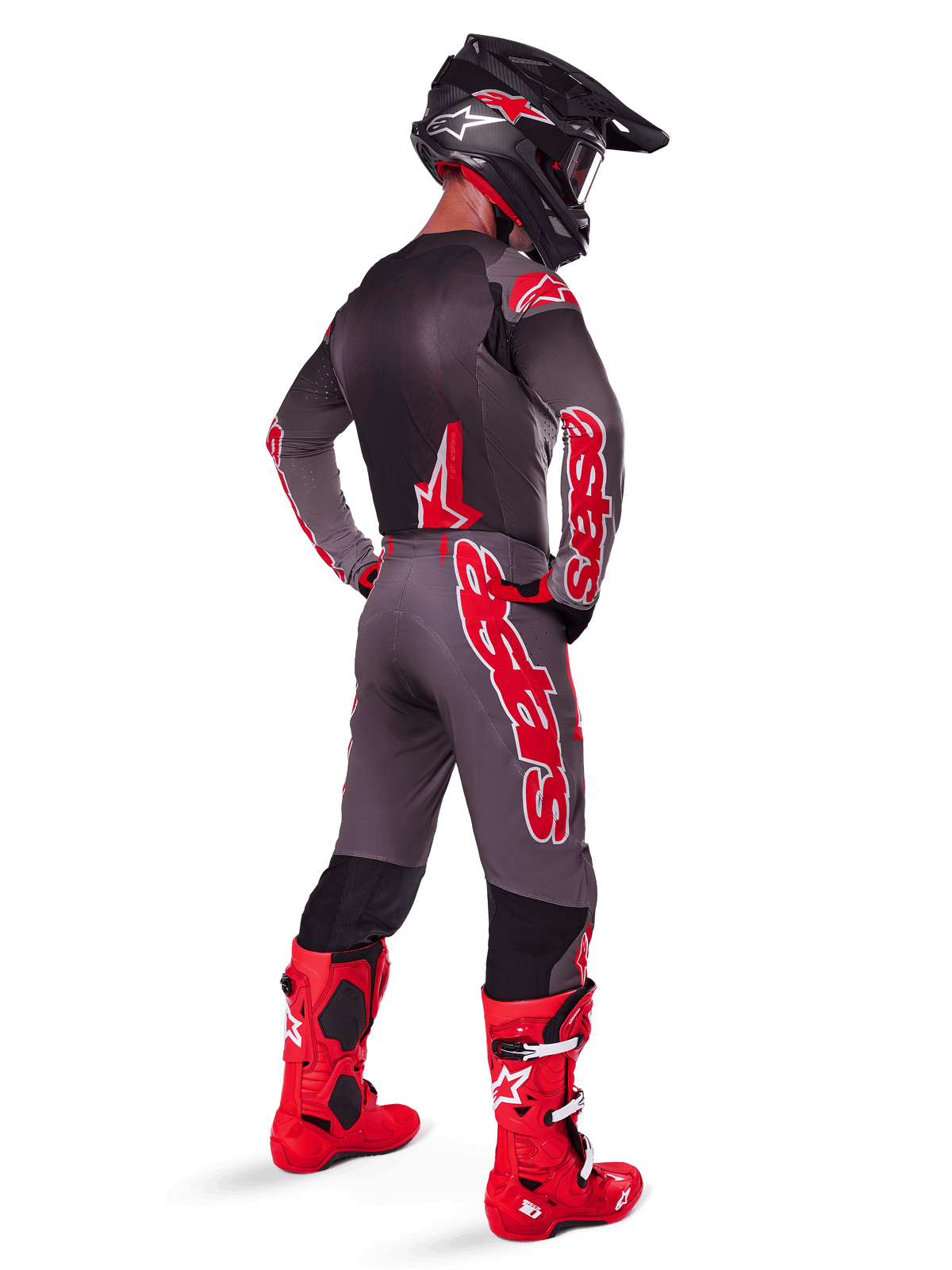 Pilote de motocross portant le maillot Supertech Lipan 2025, Smoke Bright Red, vu de dos avec un pantalon assorti gris et rouge, des bottes rouge vif, un casque noir avec des accents rouges et des lunettes rouges, ensemble d'équipement professionnel coordonné pour la course tout-terrain