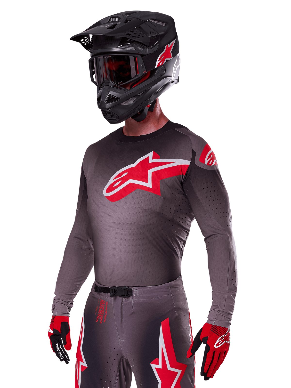 Alpinestars 2025 Supertech Lipan Gear Set, motorcrossrijder in een donkergrijze jersey en broek met rode en witte accenten, met een groot rood Alpinestars-logo op de borst, laser-gesneden perforaties voor ventilatie, bijpassende zwarte helm, rode bril en rood-zwarte handschoenen.