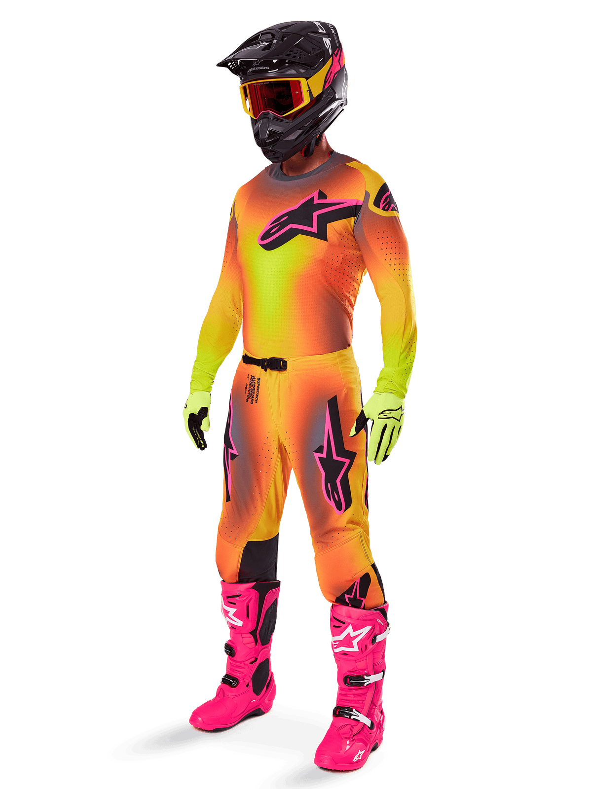 Motorcrossrijder in de 2025 Alpinestars Supertech Lipan gearset, jersey en broek met geel en oranje kleurverloop en roze accenten, zwarte helm met geel-rode crossbril, felgele handschoenen en felroze laarzen, gecoördineerde off-road race-outfit