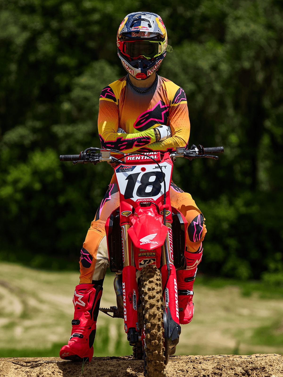 Motorcrossrijder op een rode Honda crossmotor met startnummer 18, draagt Alpinestars 2025 Supertech Lipan Jersey en bijpassende broek in geel en roze, felroze Alpinestars laarzen, Red Bull helm, professionele race-uitrusting voor off-road prestaties