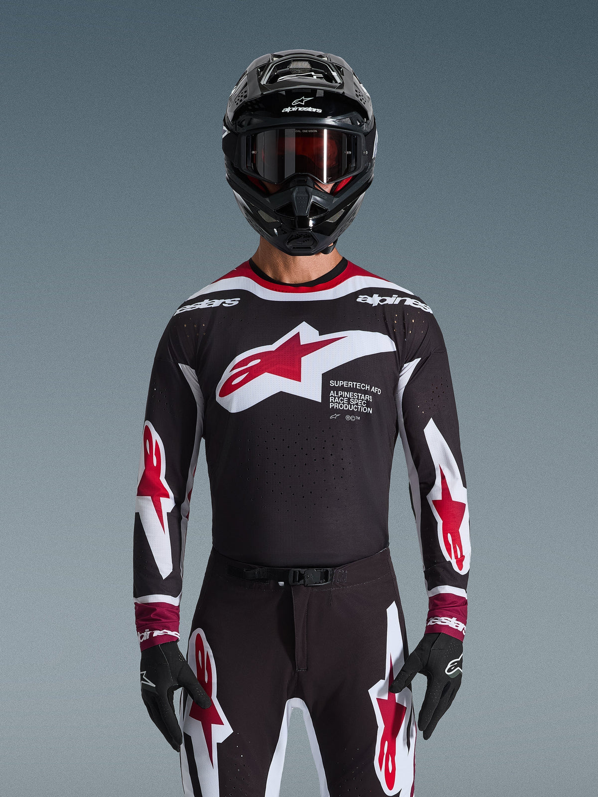 Alpinestars 2026 Supertech AFD Vista Jersey, motorcross shirt in zwart, rood en wit, getoond op een rijder met een zwarte helm, crossbril en handschoenen, voorzien van een groot logo op de borst en 'SUPERTECH AFD' branding, professionele racekleding voor off-road prestaties