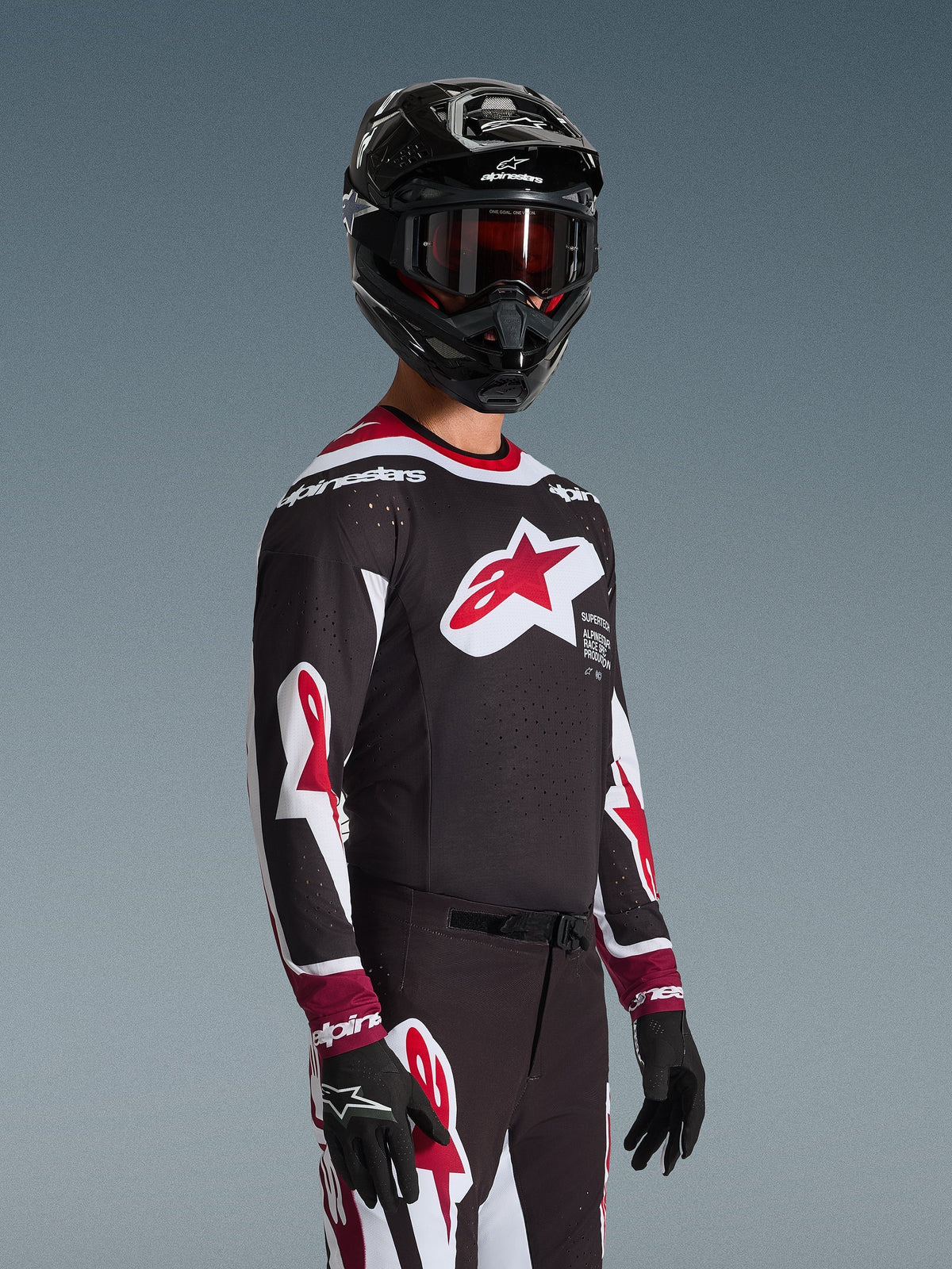 Alpinestars 2026 Supertech AFD Vista Jersey, Motocross rider wearing complete racing gear, Black jersey with red and white accents, large logo on chest, laser-cut perforations, worn with matching pants, black helmet, and red goggles, coordinated outfit for off-road racing