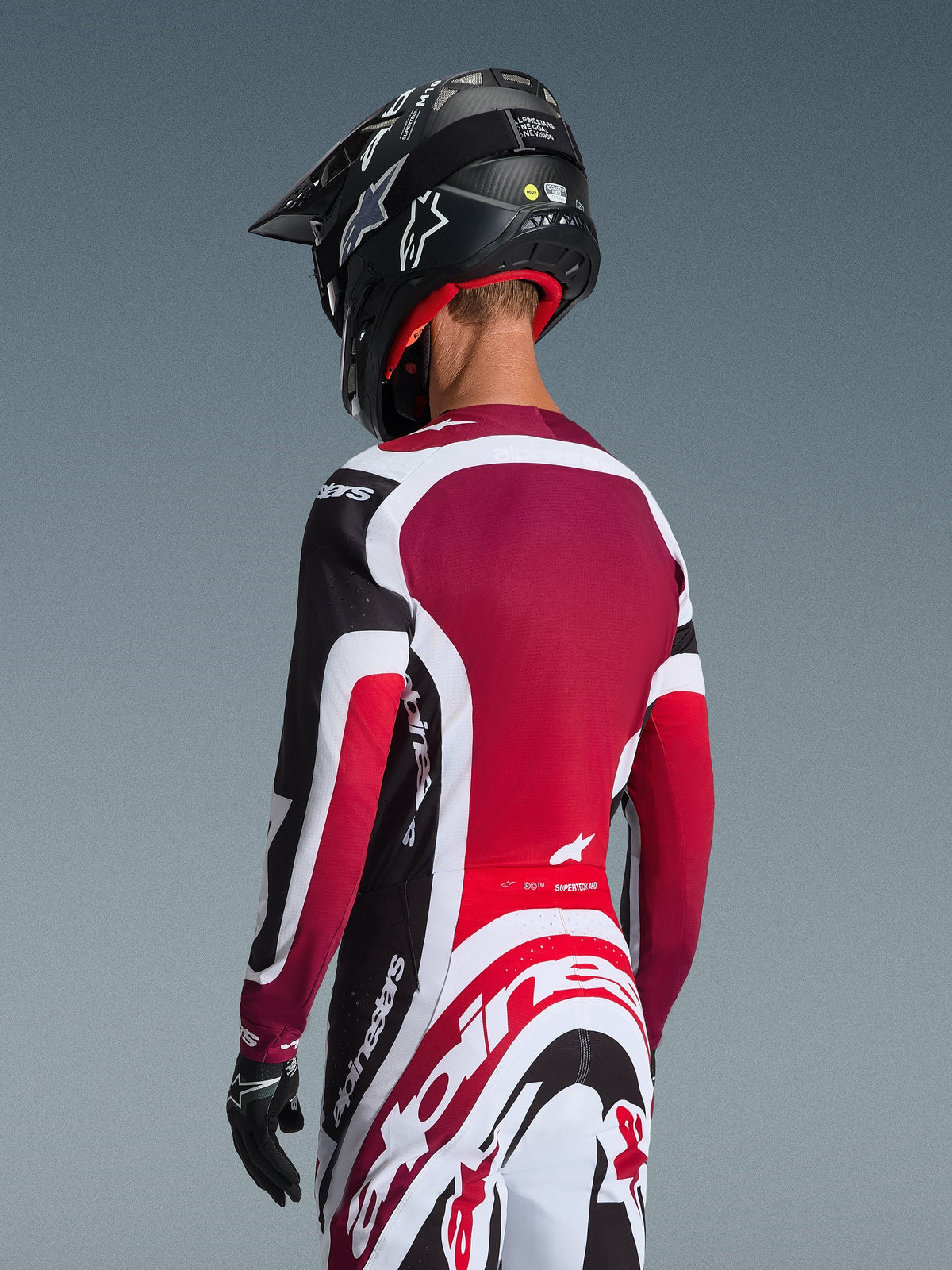 Alpinestars 2026 Supertech AFD Vista Gear Set, back view of a motocross rider in black, red, and white racing apparel, jersey with deep red back panel and athletic fit, matching pants with bold Alpinestars logo, black helmet and gloves, professional motocross racing outfit
