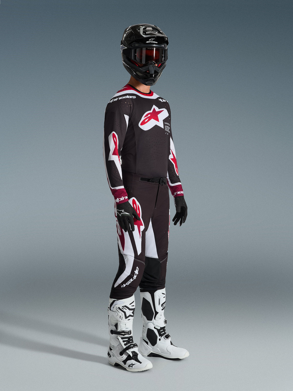 Alpinestars 2026 Supertech AFD Vista Gear Set, Motocross rider in full racing apparel, black jersey with large red star logo on the chest, matching black pants with red and white details, white and black motocross boots, black helmet with red goggles, professional motocross racing outfit