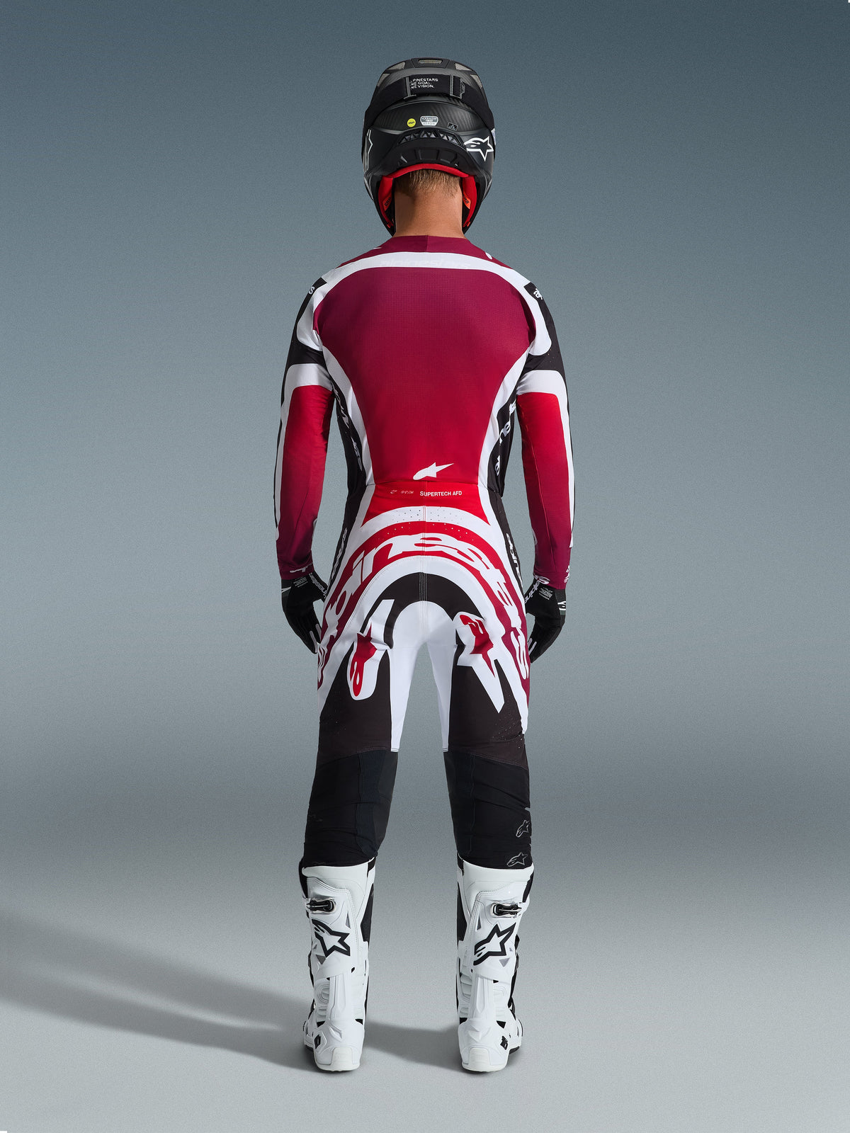 Alpinestars 2026 Supertech AFD Vista Gear Set, Rear view of a motocross rider in professional racing gear, burgundy and red jersey with white and black accents, matching pants with bold graphics, white boots, and black helmet, coordinated motocross racing outfit.