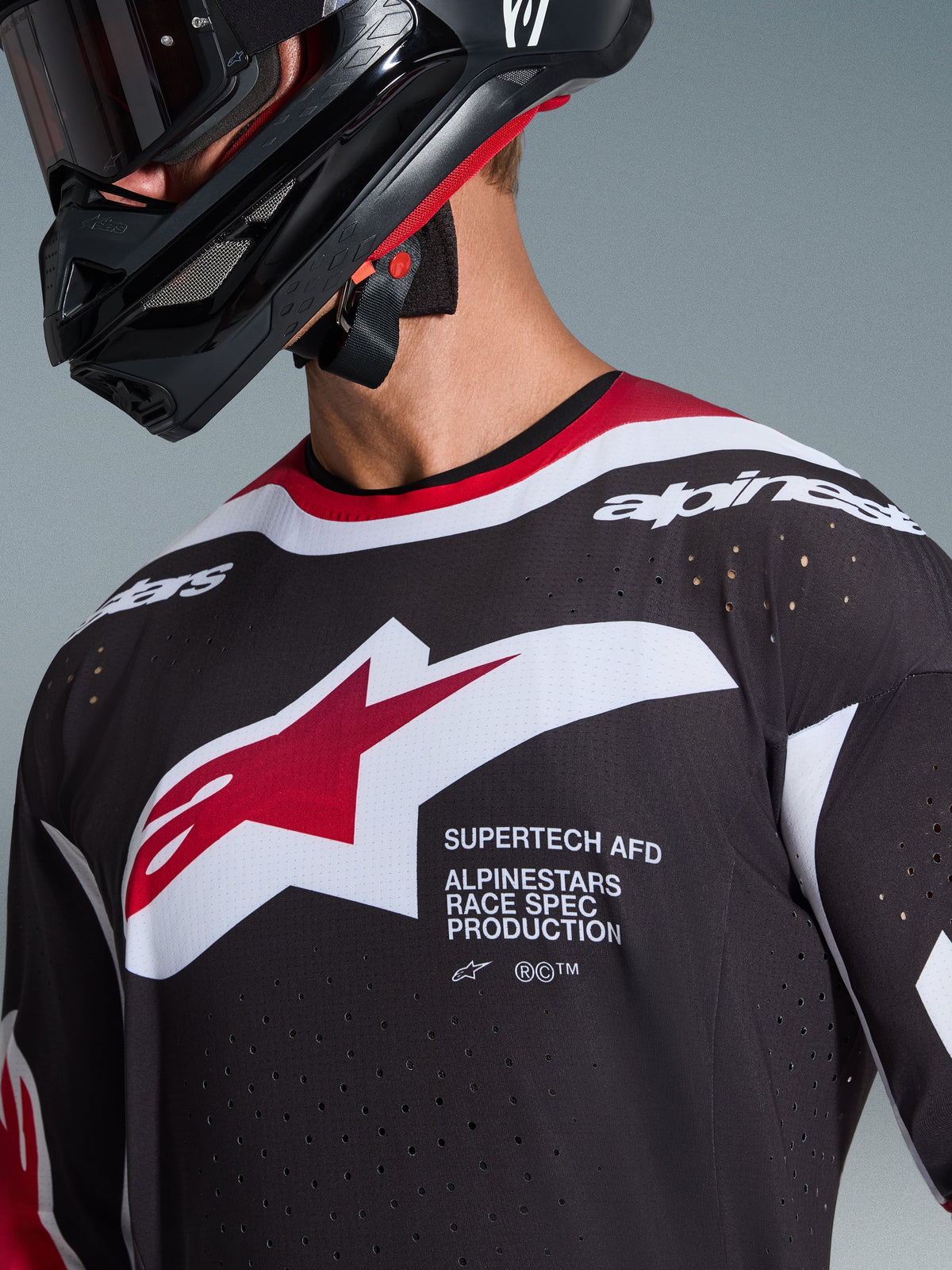 Alpinestars 2026 Supertech AFD Vista Jersey, close-up van een motorcrossrijder in een zwart shirt met rode en witte accenten, voorzien van een groot wit en rood Alpinestars-logo, laser-gesneden ventilatieperforaties en een professionele racepasvorm, gecombineerd met een zwarte helm.