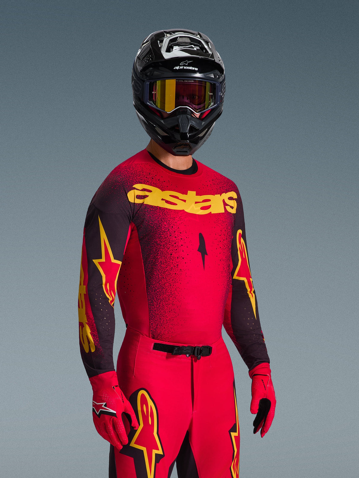 Pilote de motocross portant le maillot Alpinestars Supertech Scenz 2026 rouge et noir avec logo 'astars' jaune, pantalon et gants rouges assortis, casque noir avec lunettes, équipement de course professionnel pour le motocross tout-terrain