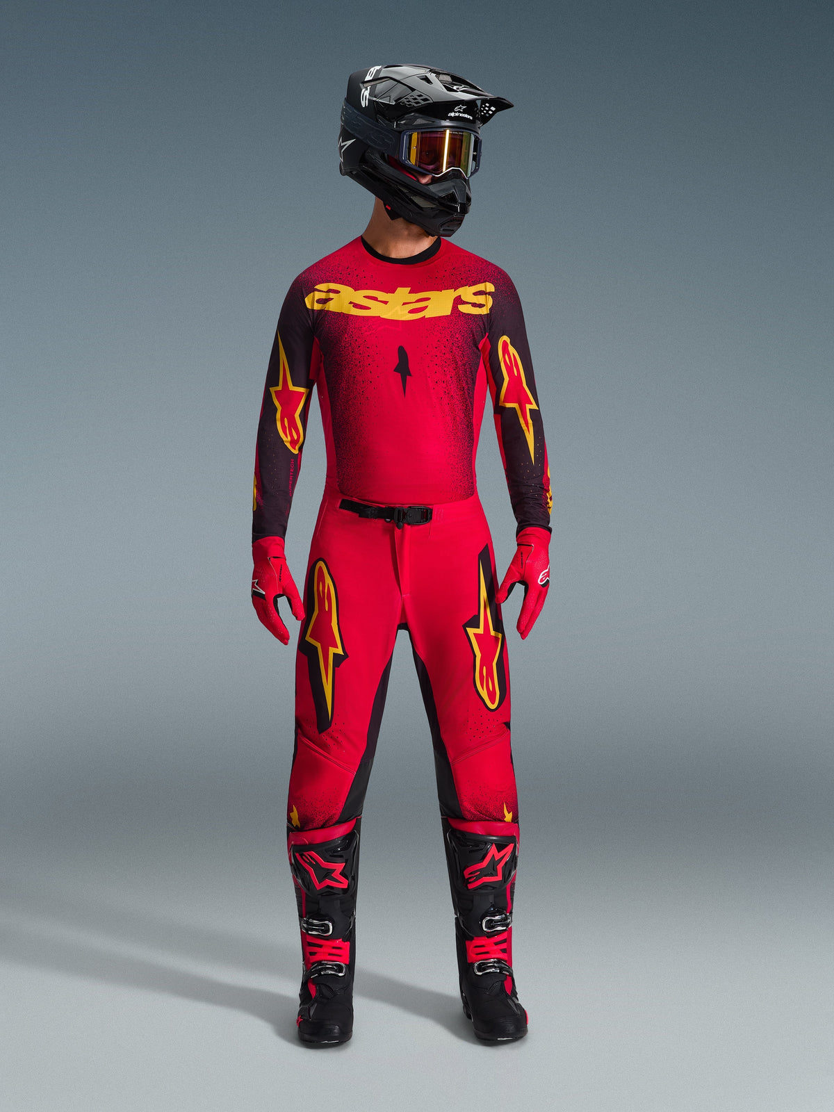 Pilote de motocross portant le maillot Alpinestars 2026 Supertech Scenz en Rouge Noir Jaune, avec pantalon assorti, casque noir et lunettes, gants rouges et bottes noires et rouges, ensemble d'équipement de course professionnel pour la performance tout-terrain
