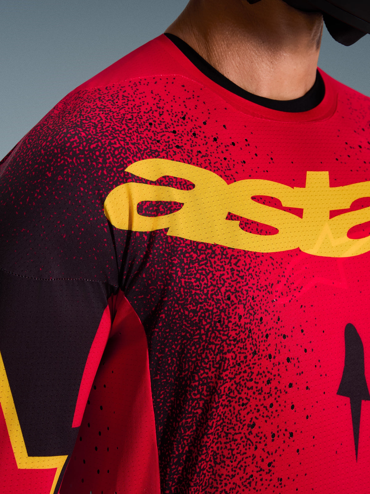 Maillot Alpinestars Supertech Scenz 2026, maillot de motocross, rouge, noir et jaune, gros plan sur la poitrine avec logo jaune, motif tacheté noir et perforations laser pour la ventilation.