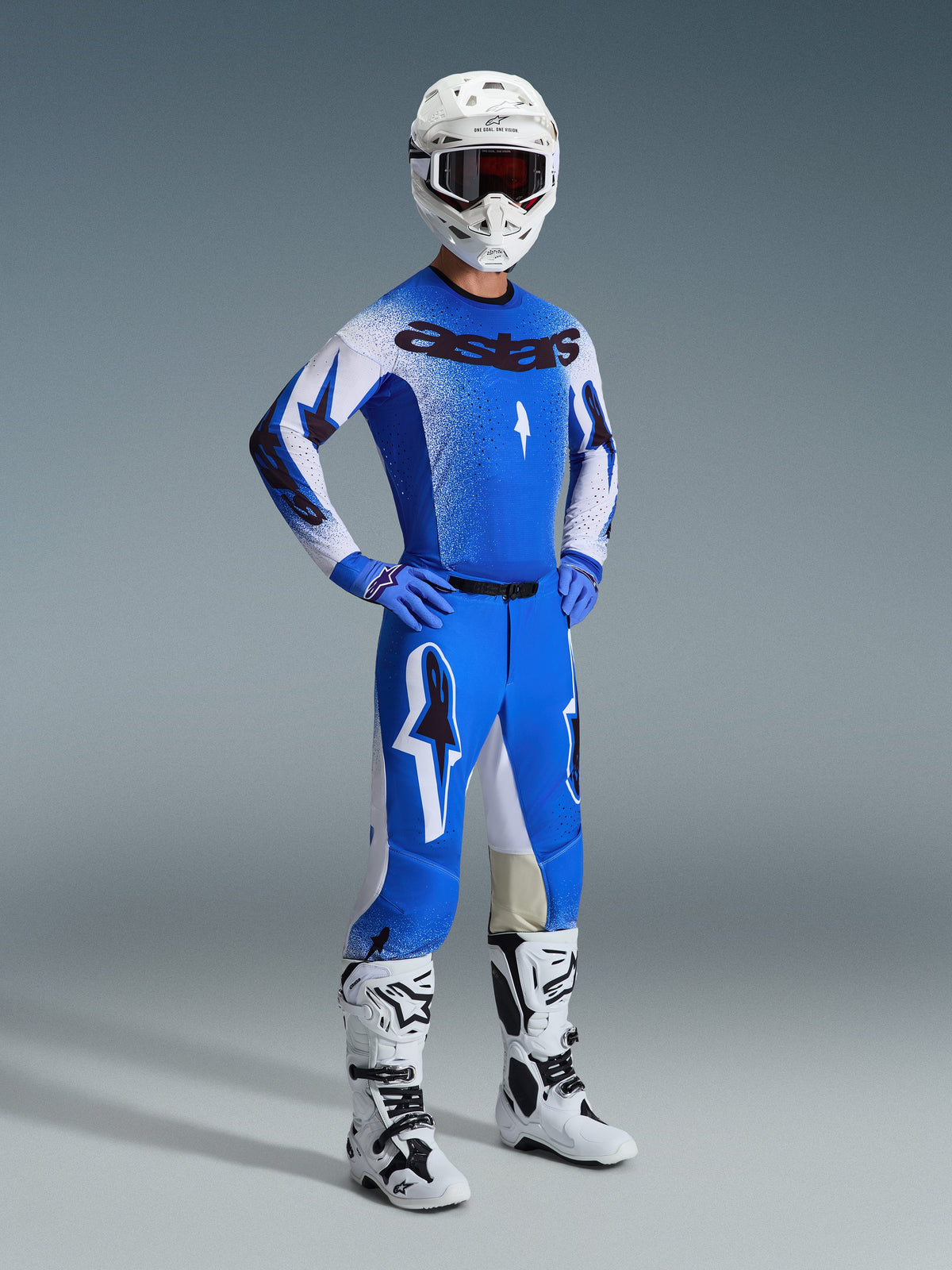 Pilote de motocross portant l'ensemble d'équipement Alpinestars 2026 Supertech Scenz en bleu Ucla et blanc, comprenant un maillot professionnel avec marquage 'astars', un pantalon de performance assorti, un casque blanc, des lunettes sombres et des bottes tout-terrain blanches et noires.