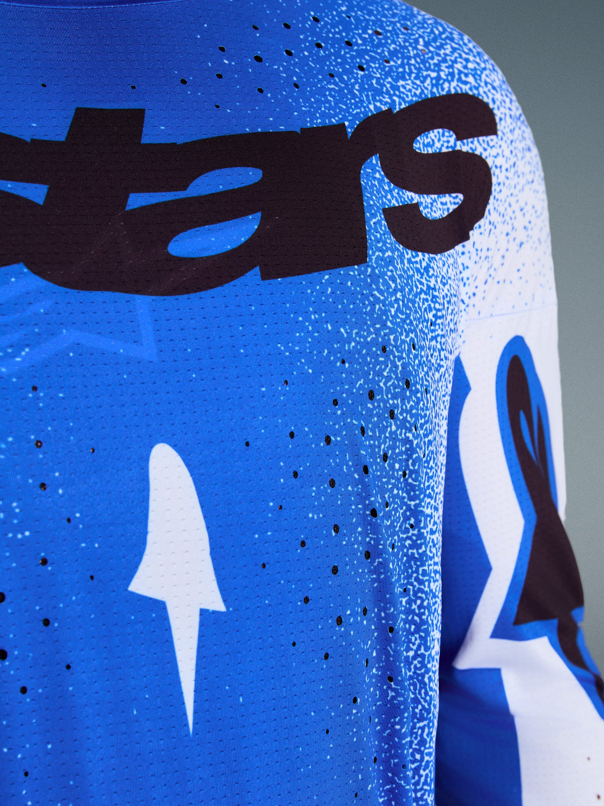 Maillot Alpinestars Supertech Scenz 2026, gros plan sur le design Bleu UCLA et blanc, avec perforations au laser pour la ventilation, marquage 'stars' noir et tissu en maille respirante pour le motocross professionnel.