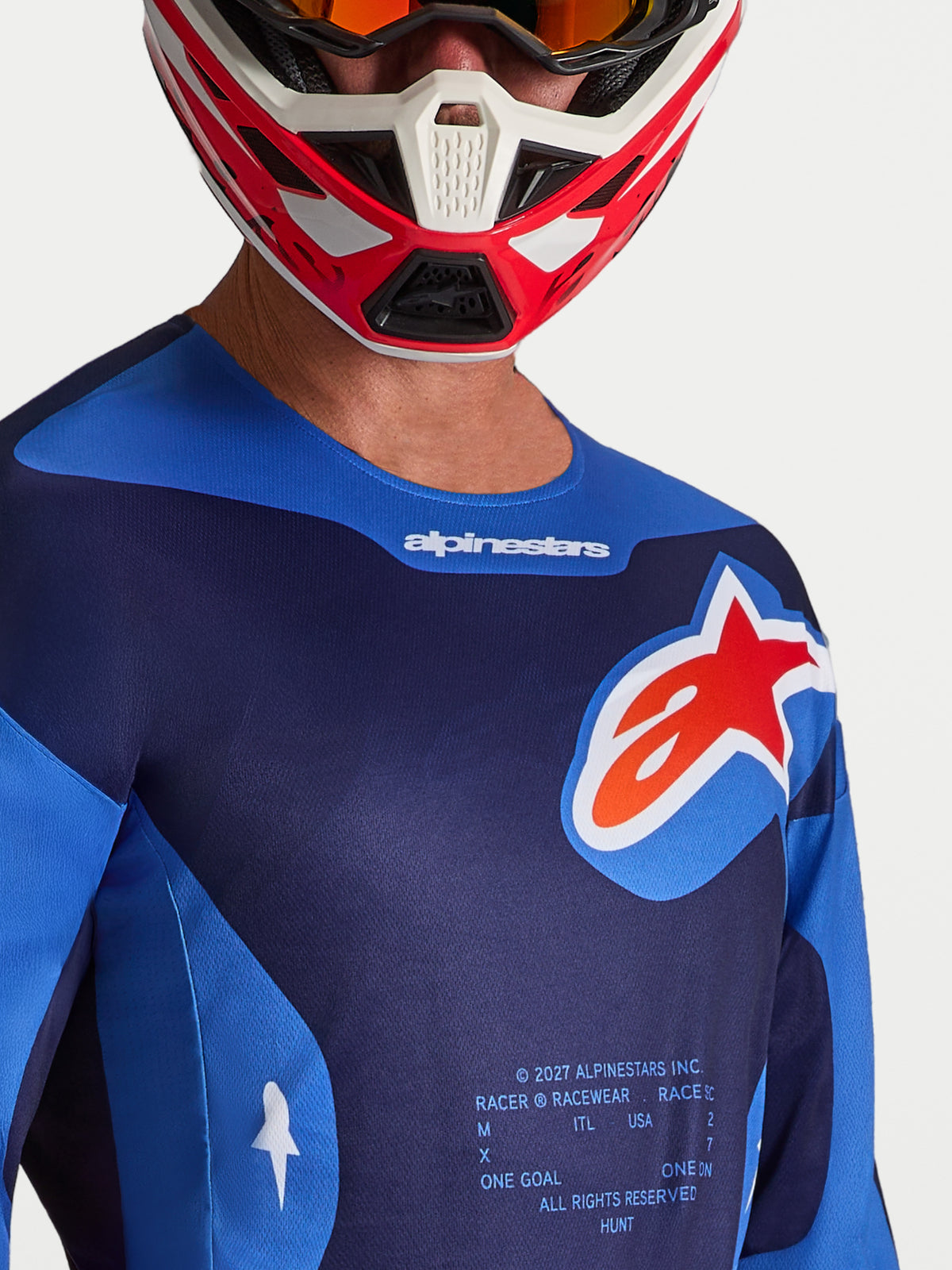 Alpinestars Racer Hunt Jersey, heren-motocrossjersey, blauw en rood, vochtafvoerend polyfabric met groot logo op de borst, gedragen door een rijder met helm.