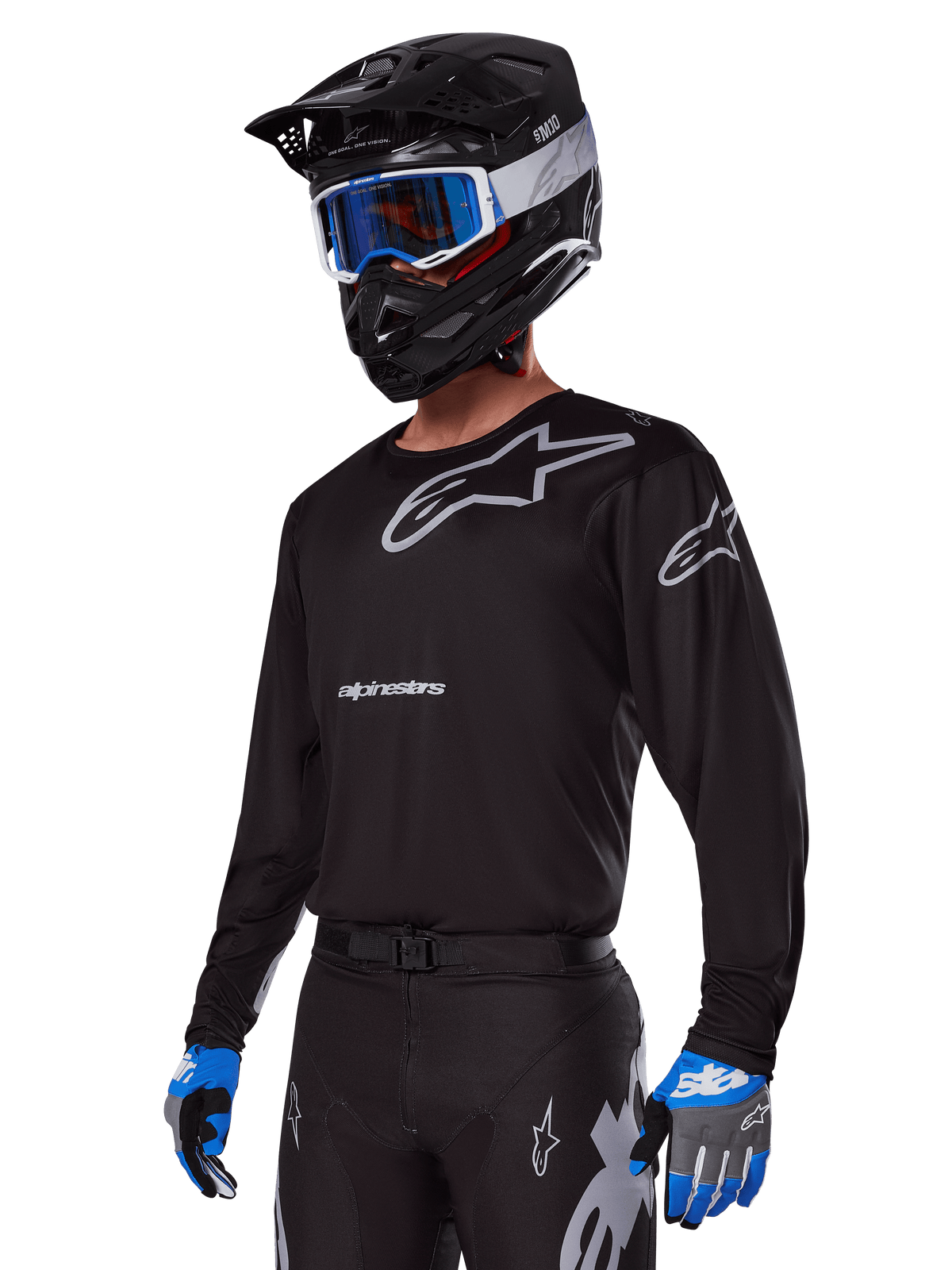 Motocross-Fahrer im Alpinestars 2025 Racer Graphite Ausrüstungsset, schwarzes Jersey mit grauen Alpinestars-Logos, passende schwarze Hose mit grauen Akzenten, schwarzer Helm mit blau-weißer Brille, blau-graue Handschuhe, elegantes technisches Outfit für Offroad-Rennsport