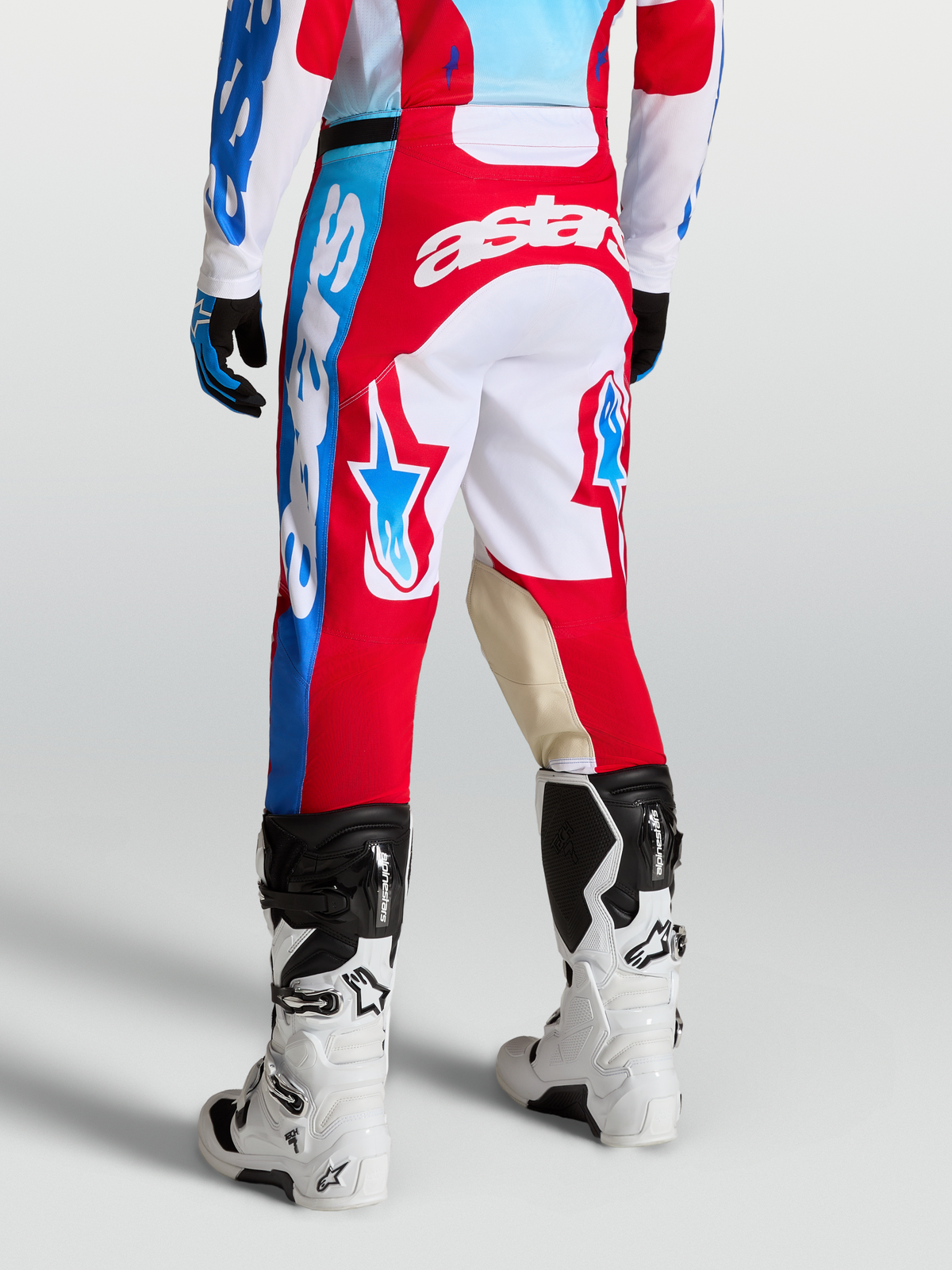 Alpinestars Pantalons Racer Hunt, pantalons de motocross rouges et blancs portés par un mannequin, graphismes étoiles et logos, empiècements genoux en cuir de chèvre, coupe sport ergonomique.