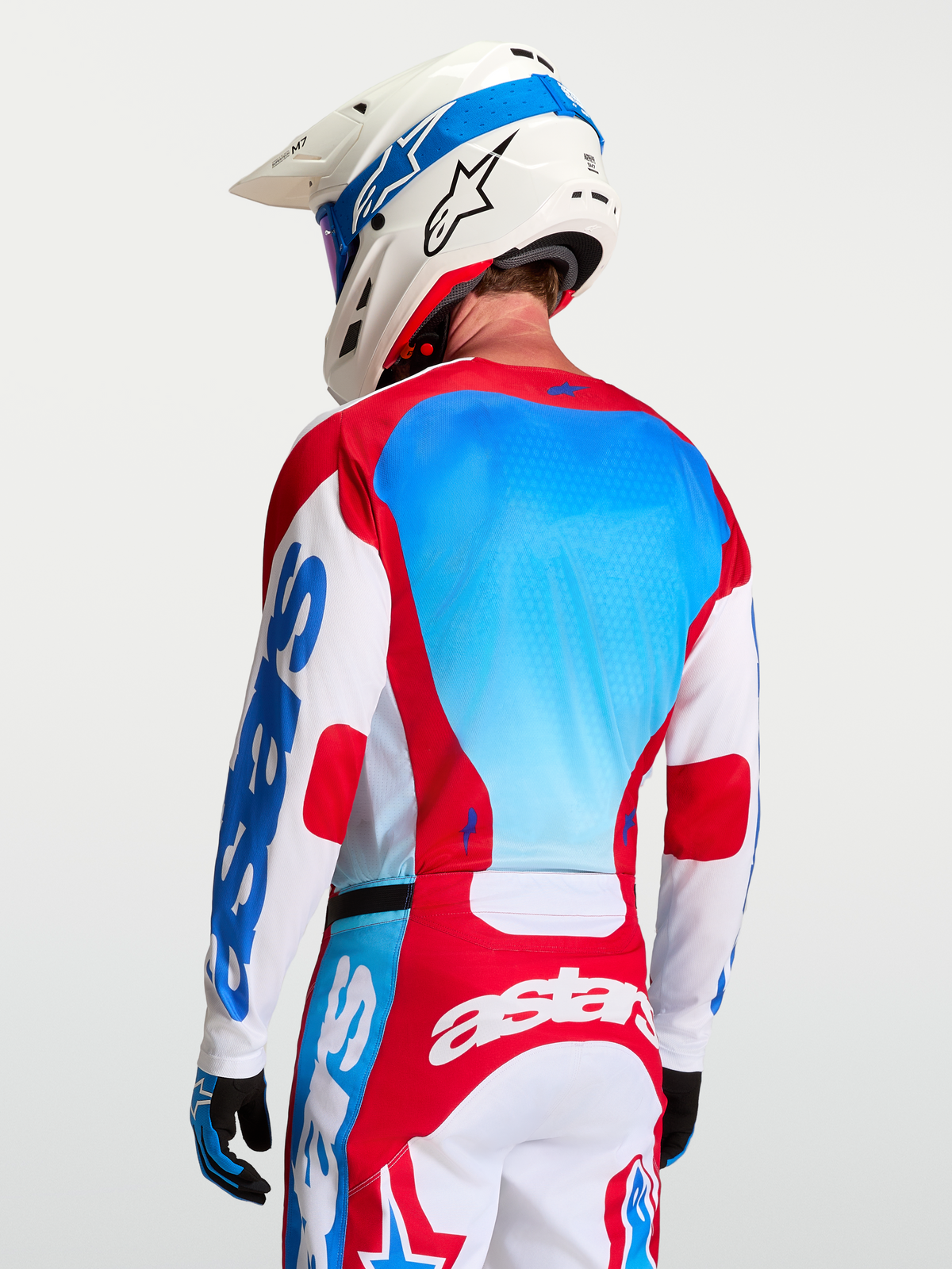 Alpinestars Racer Hunt motorcrossjersey in wit, rood en blauw met mesh-panelen op de rug en racepasvorm op een model.