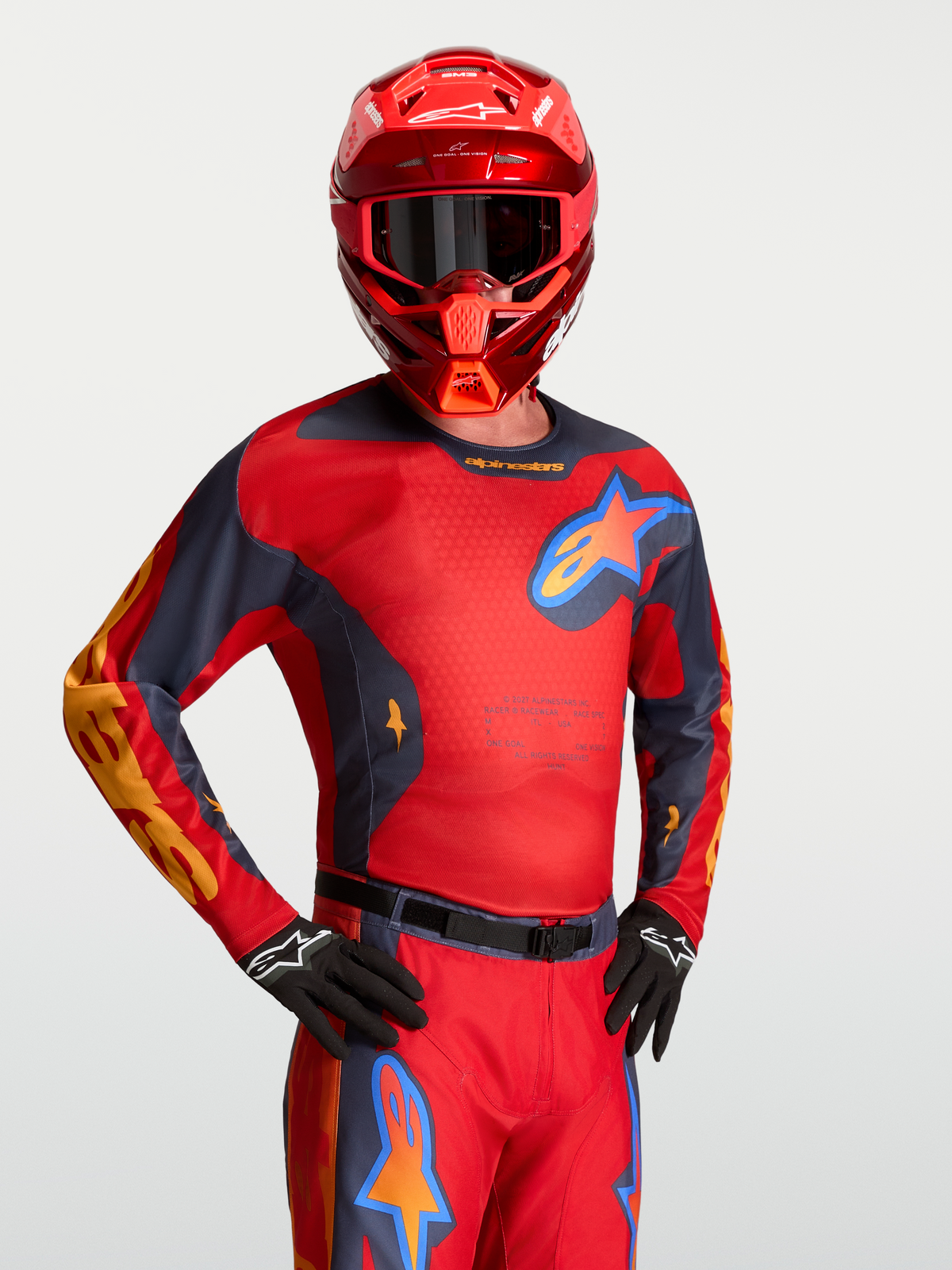 Maillot Alpinestars Racer Hunt, haut de motocross rouge et gris avec panneaux en maille, porté avec un casque assorti.