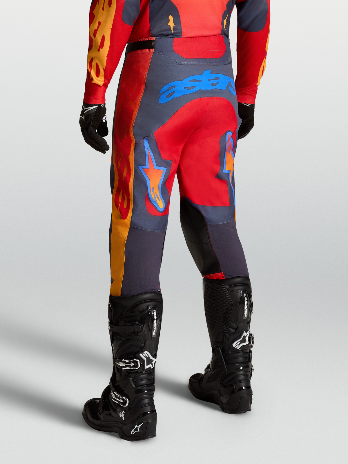 Alpinestars Pantalon Racer Hunt, pantalon de motocross performance, rouge et gris, vue arrière sur mannequin en bottes, inserts en tissu ripstop extensible et genoux renforcés pour la course off-road