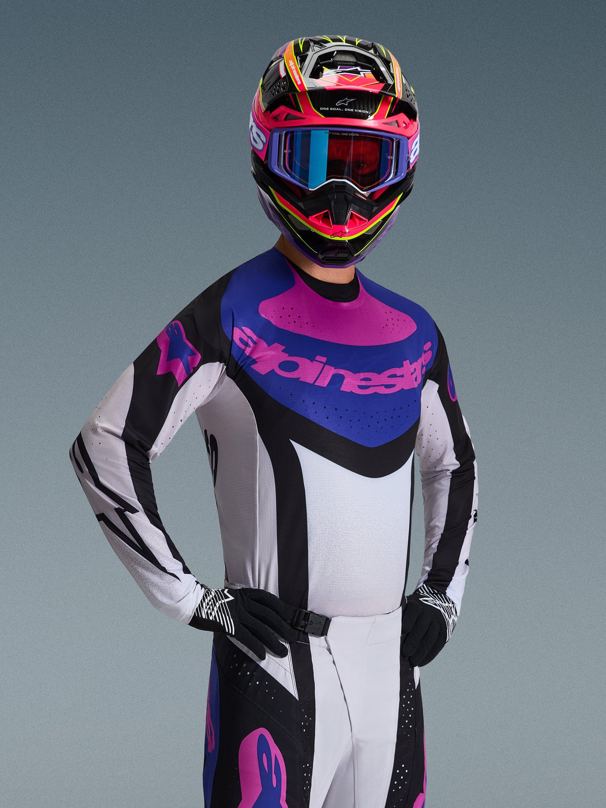 Alpinestars 2026 Techstar Knif Jersey, Motocross-Trikot, Schwarz, Hellgrau und Lila, getragen von einem Fahrer in kompletter Ausrüstung, weißes Chassis mit schwarzen Akzenten und blauem Brustpanel mit lilafarbenem Alpinestars-Logo, Hochleistungs-Rennpassform für den Offroad-Sport.