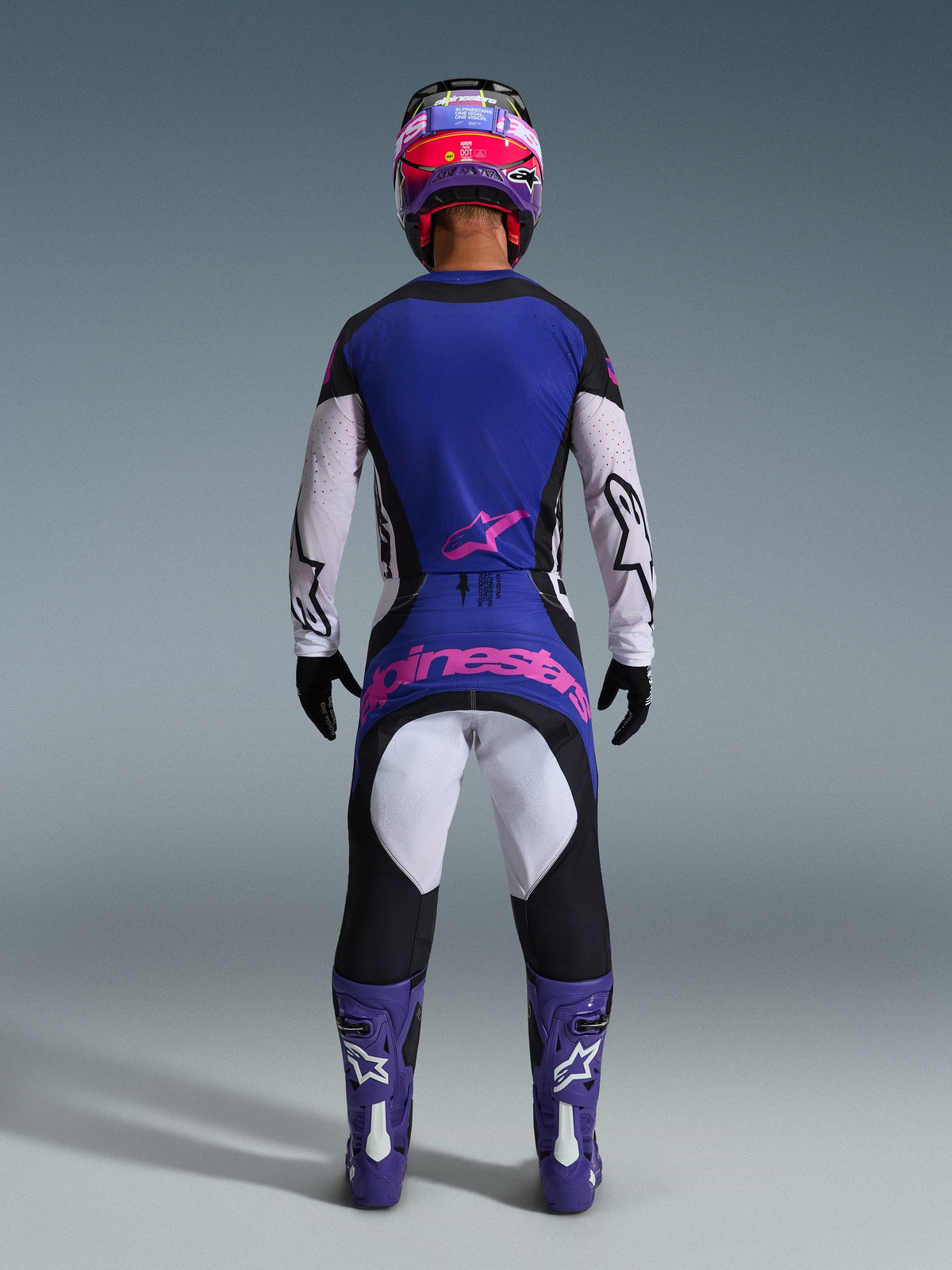 Motocross-Fahrer in der Rückansicht mit dem 2026 Techstar Knif Jersey, Schwarz-Hellgrau-Lila, passende Motocross-Hose mit pinkfarbenem Branding, lila Stiefel und Helm, koordinierte Hochleistungs-Offroad-Ausrüstung