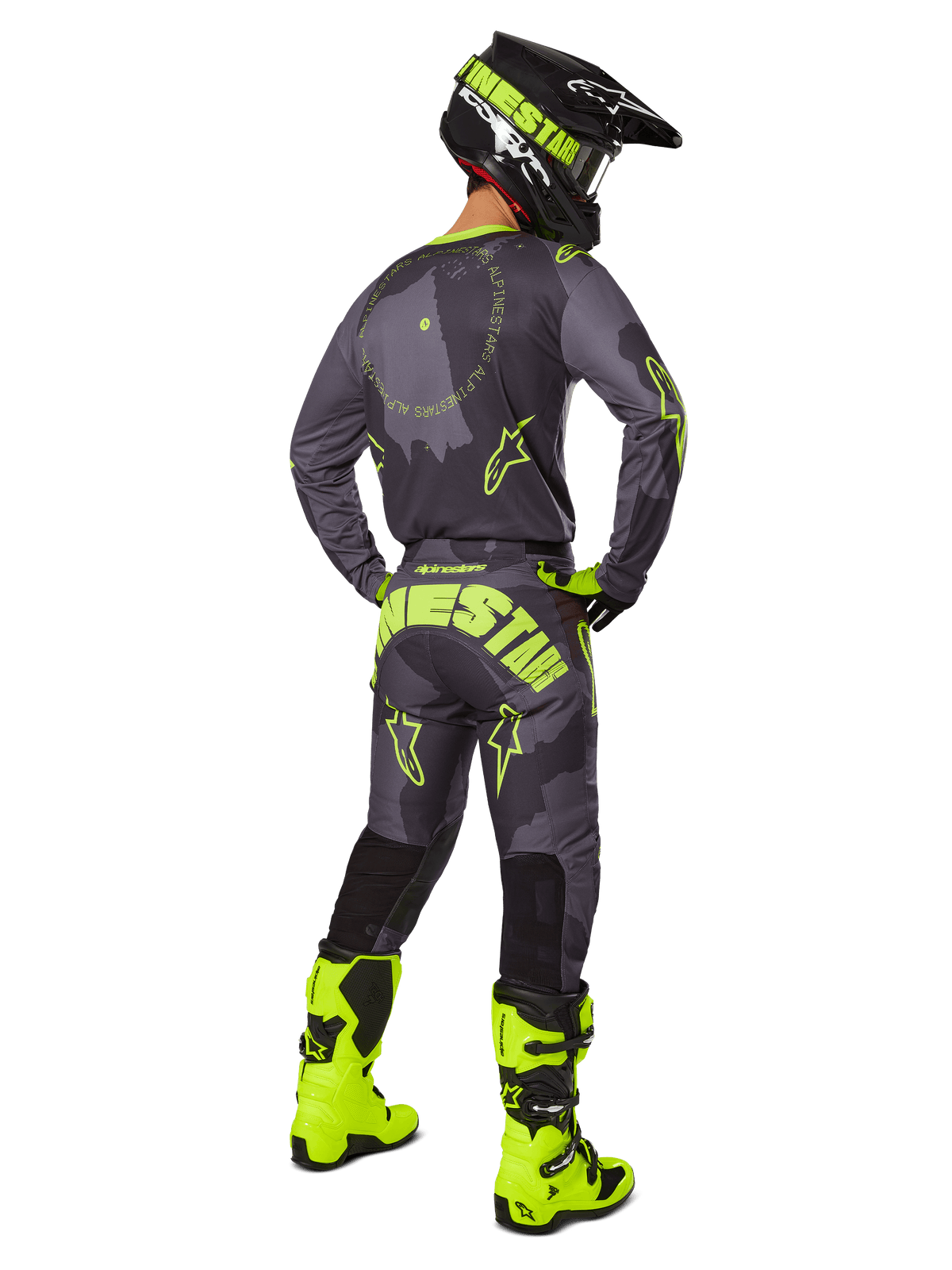 Pilote de motocross de dos portant le maillot et le pantalon Alpinestars Racer Hollow 2025 en coloris Dark Camo Yellow Fluo, avec un motif camouflage gris foncé et des accents jaune fluo, assorti à un casque noir et jaune et des bottes jaune fluo éclatantes.