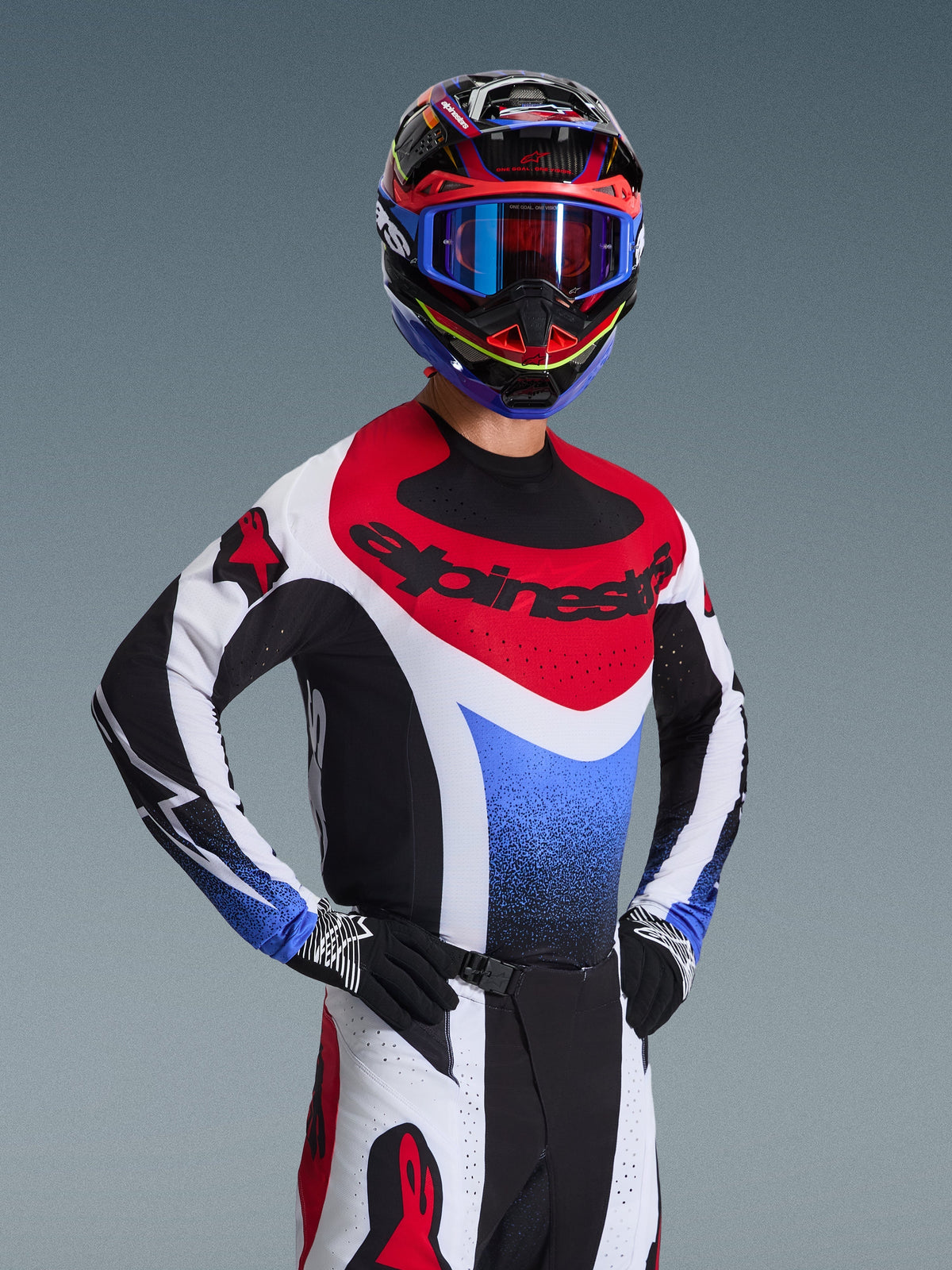 Motocross-Fahrer im Alpinestars 2026 Techstar Knif Trikot in Rot, Weiß und Blau, mit schwarzem Branding auf der Brust, passender Motocross-Hose, abgestimmtem Rennhelm mit blauer Brille und schwarz-weißen Handschuhen, professionelle Offroad-Ausrüstung für den Wettkampf