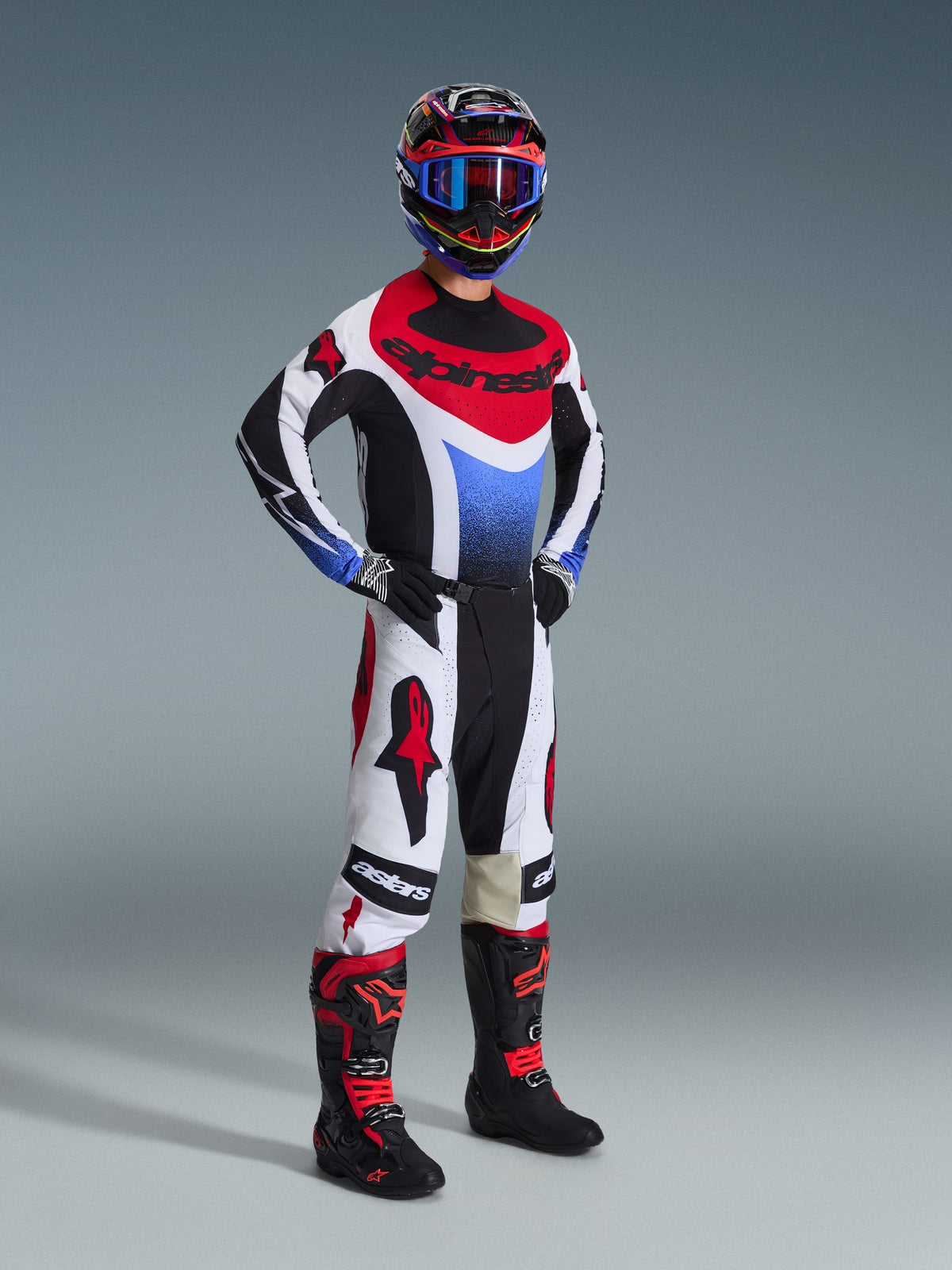 Motocross-Fahrer im 2026 Techstar Knif Trikot in Schwarz, Weiß und Rot mit blauen Akzenten, kombiniert mit passender weißer und roter Hose, schwarz-roten Stiefeln und einem Helm mit blauer Brille, komplette Offroad-Rennausrüstung