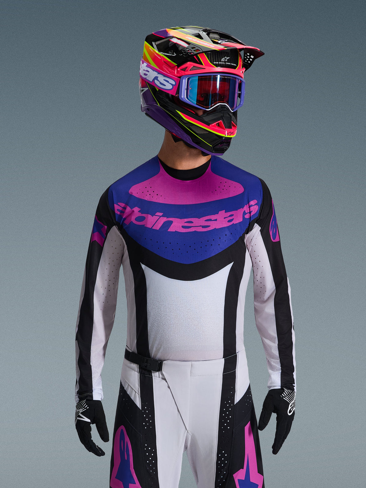 Alpinestars 2026 Techstar Knif Jersey, Motocross-Trikot, Schwarz, Hellgrau und Lila, pinkfarbenes Alpinestars-Logo auf der Brust, getragen mit passendem bunten Helm und Motocross-Hose, athletische Rennpassform mit lasergeschnittenen Perforationen zur Belüftung