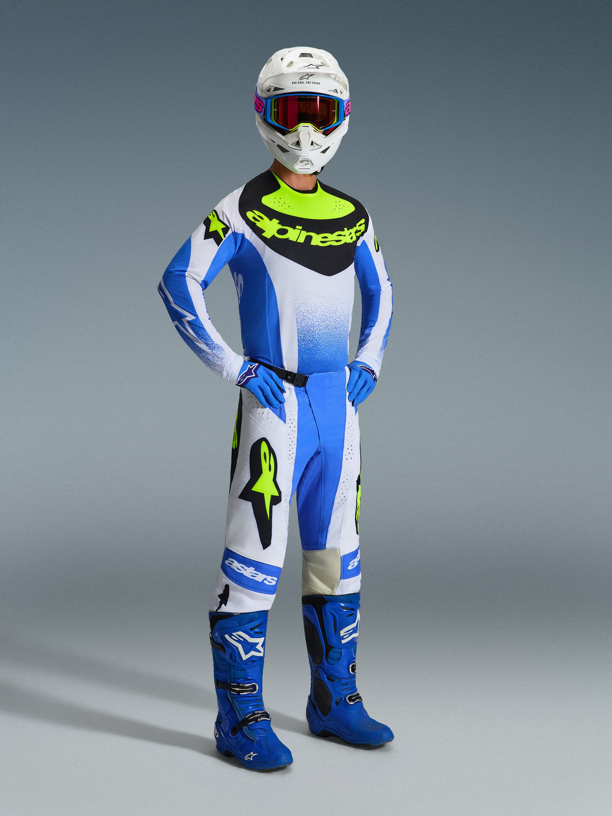 Motocross-Fahrer trägt das Alpinestars 2026 Techstar Knif Gear Set in Ucla-Blau, Schwarz und Fluo-Gelb, bestehend aus einem Performance-Trikot, passender Hose mit markantem Branding, blauen Stiefeln, blauen Handschuhen und einem weißen Helm mit Schutzbrille, vor grauem Hintergrund.