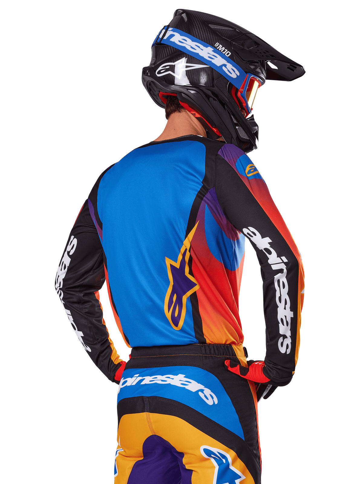 Motocross-Fahrer in der Rückansicht, Alpinestars 2025 Fluid Wurx Ausrüstungsset, mehrfarbiges Trikot mit blauem Rücken und schwarzen Ärmeln mit weißen Logos, passende orange-blaue Hose, schwarz-blauer Helm mit orangefarbener Schutzbrille, koordiniertes Offroad-Rennoutfit.