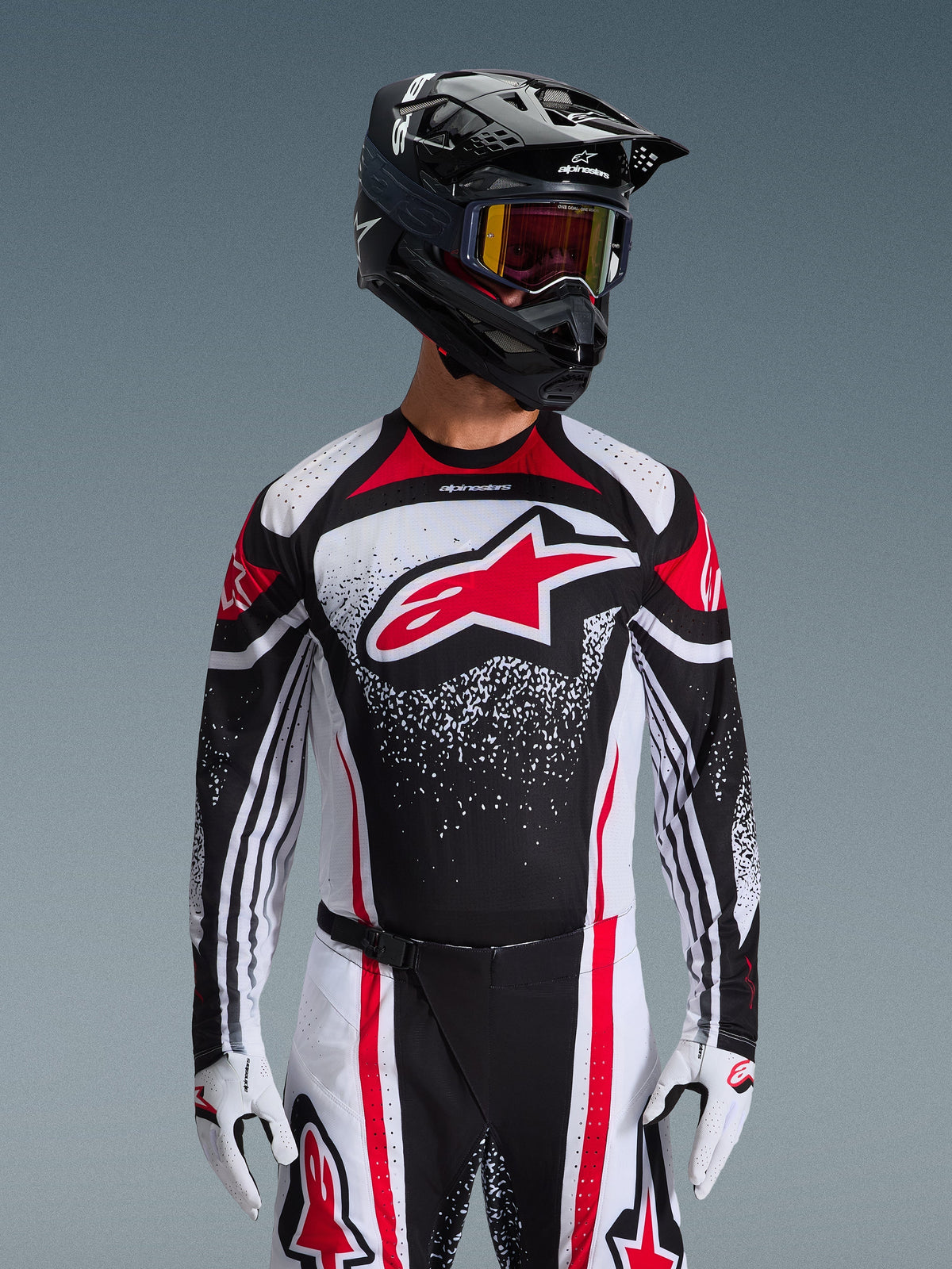 Alpinestars 2026 Techstar Nomur Trikot, Motocross-Trikot, Schwarz, Weiß und Rot, getragen von einem Fahrer mit passender Hose, schwarzem Helm und weißen Handschuhen, mit einem großen roten Astars-Logo und gesprenkeltem Grafikdesign, athletische Rennpassform für Offroad-Wettkämpfe