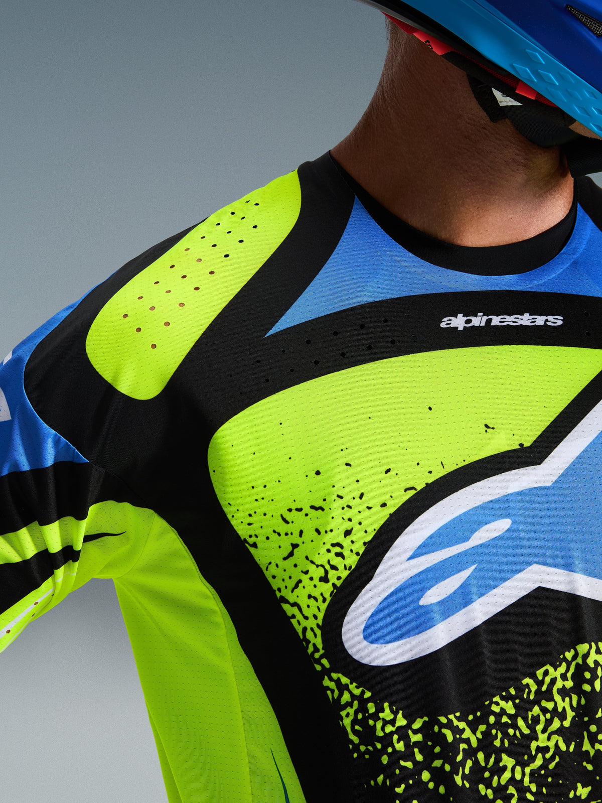 Maillot Alpinestars Techstar Nomur 2026, gros plan sur la poitrine et l'épaule en bleu marine foncé, jaune fluo et bleu, avec perforations de ventilation découpées au laser, col thermocollé sans couture et logo Alpinestars imposant, équipement de motocross haute performance.