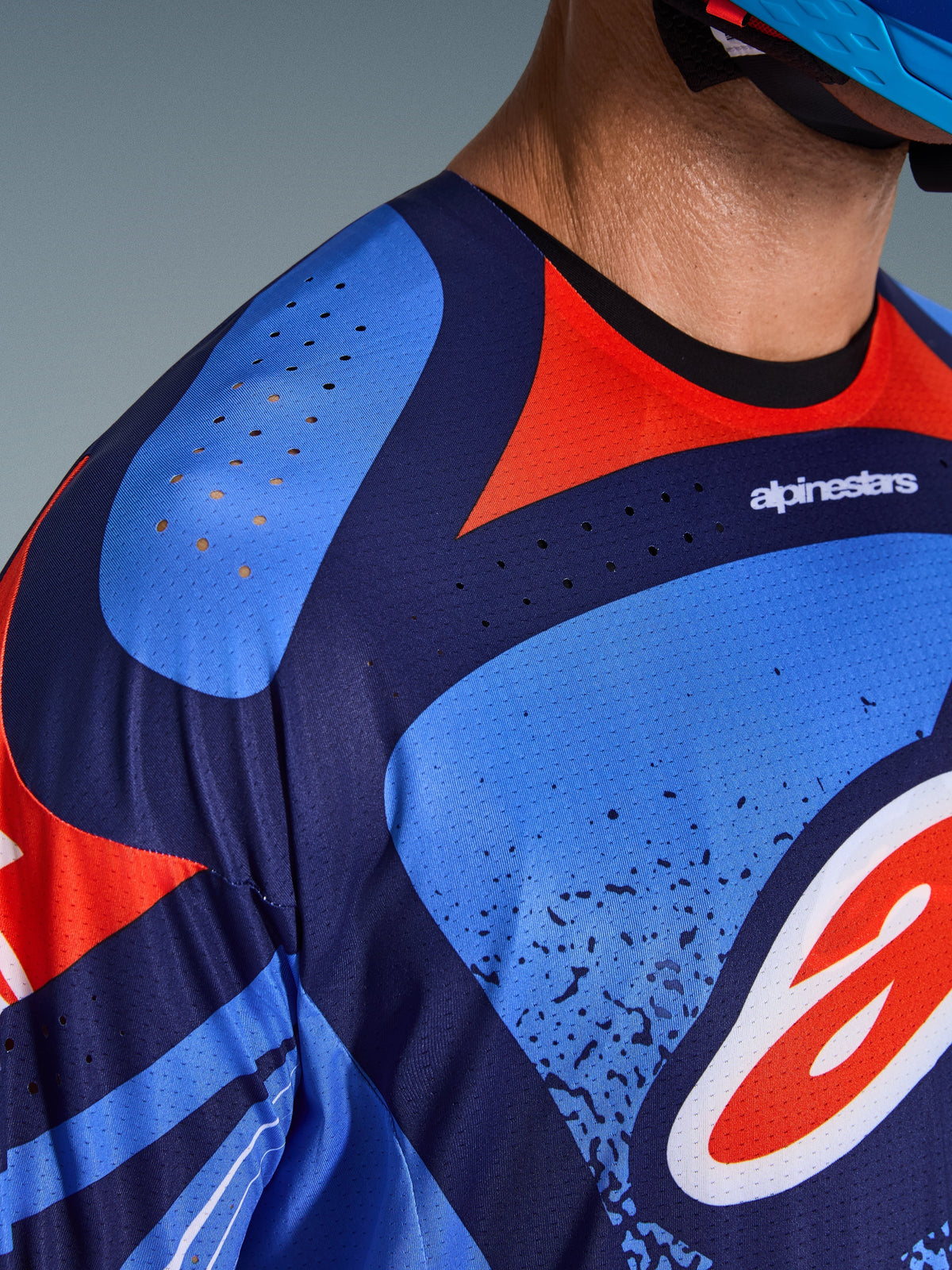 Gros plan sur le maillot Alpinestars Techstar Nomur 2026, maillot de motocross, bleu marine foncé, orange et bleu UCLA, avec perforations laser pour la ventilation sur l'épaule et la poitrine, tissu technique évacuant l'humidité, coupe athlétique de course