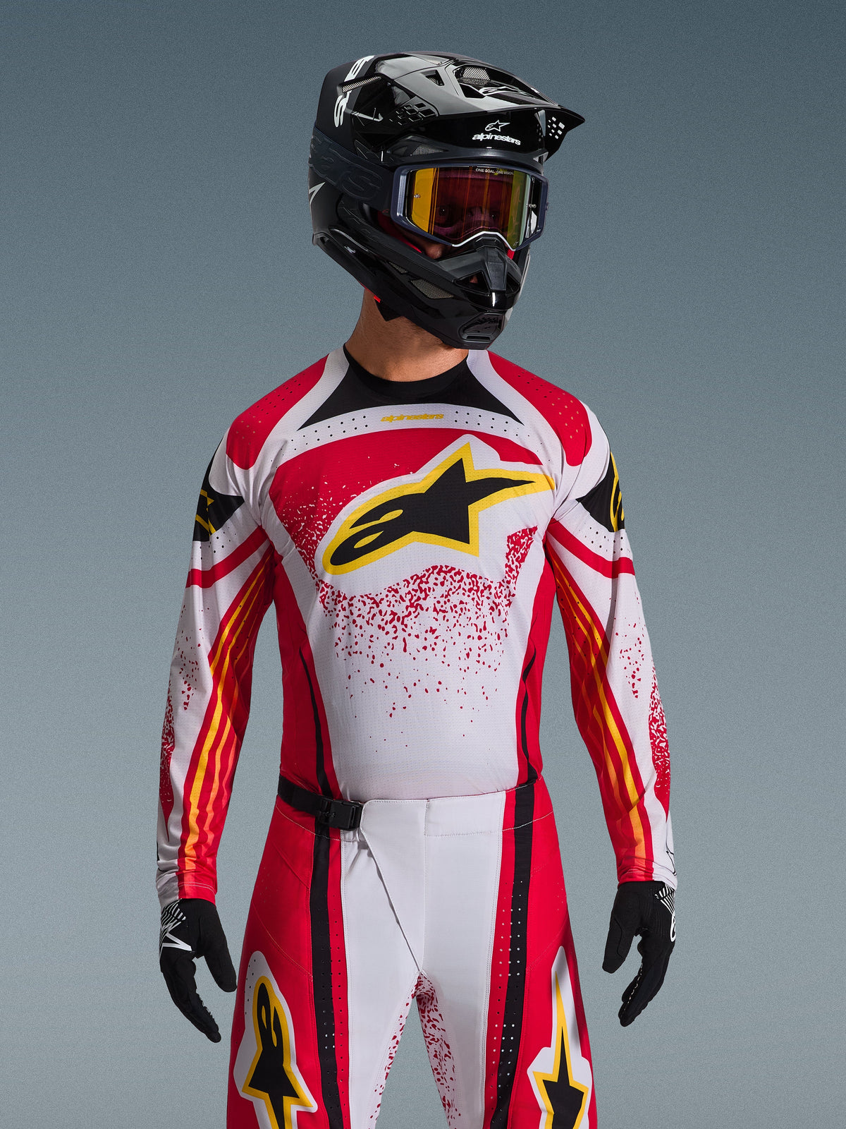 Ensemble d'équipement Alpinestars Techstar Nomur 2026, pilote de motocross portant un maillot rouge, blanc et noir avec logo jaune, pantalon assorti à motifs mouchetés, casque et lunettes noirs, gants noirs, équipement de course complet pour la compétition tout-terrain