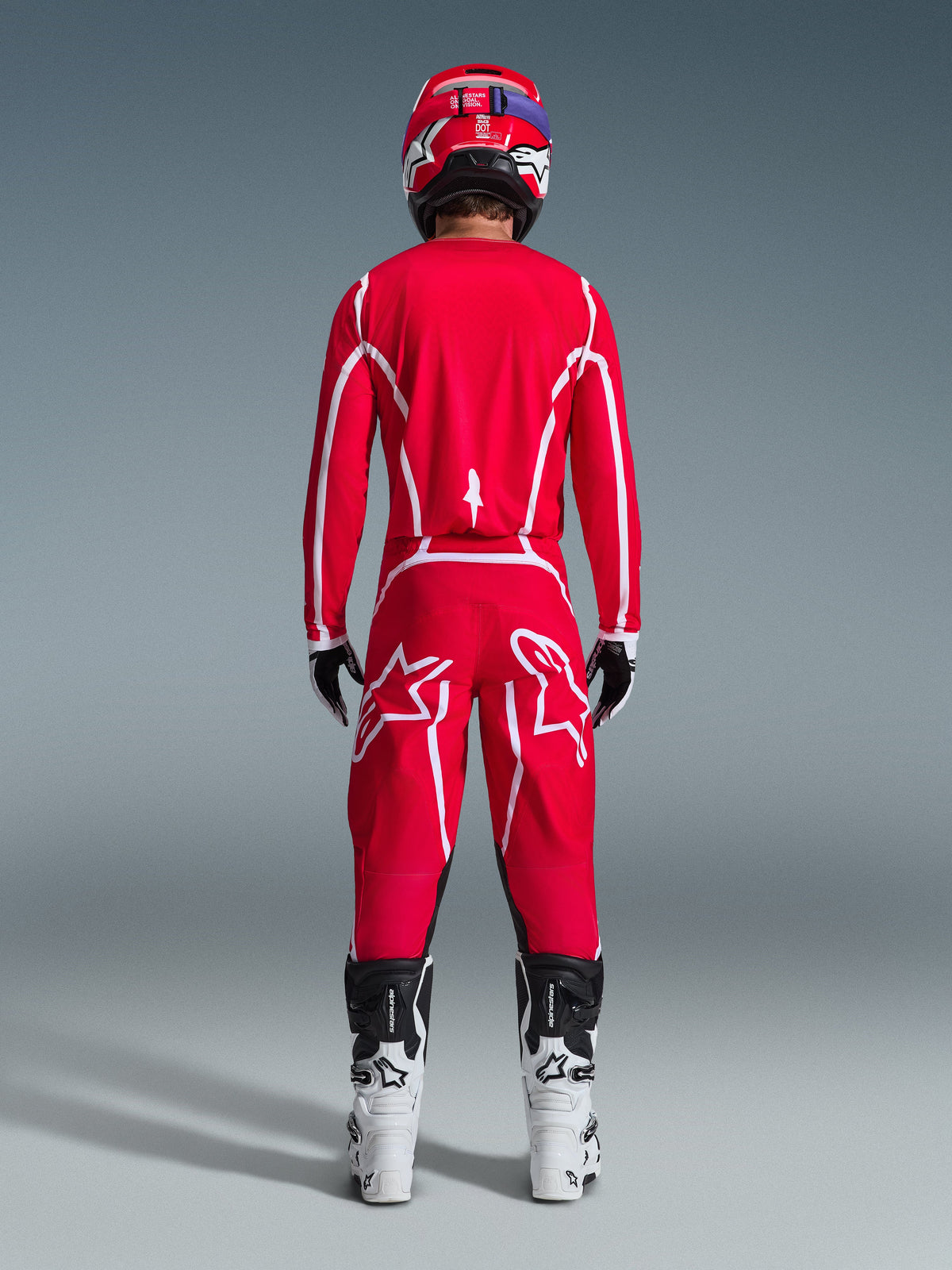 Rückansicht eines Motocross-Fahrers im Alpinestars 2026 Fluid Apex Gear Set, leuchtend rotes Jersey und Hose mit weißen Streifen und Logos, kombiniert mit weiß-schwarzen Stiefeln und einem roten Helm, professionelle Offroad-Rennausrüstung
