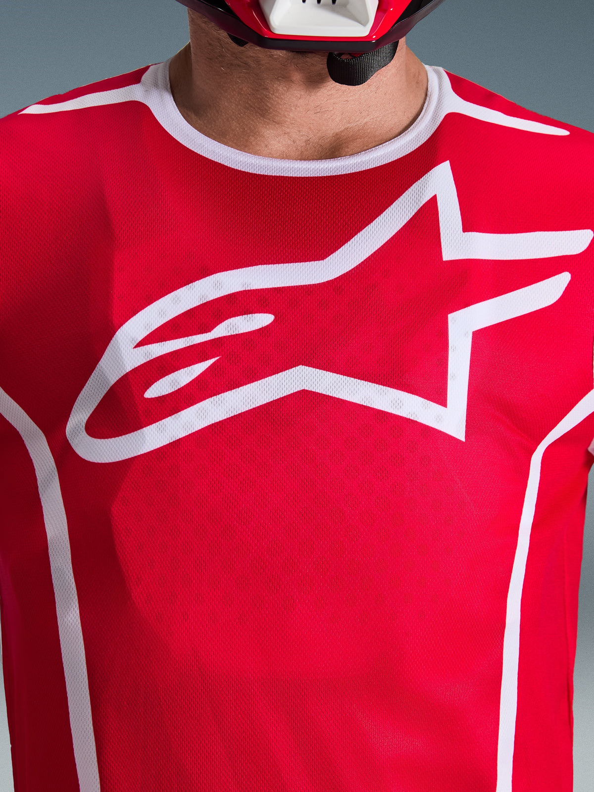 Maillot Alpinestars 2026 Fluid Apex, rouge et blanc, vue rapprochée de la poitrine avec grand logo Astars blanc, col sport blanc et tissu évacuant l'humidité pour la performance en motocross