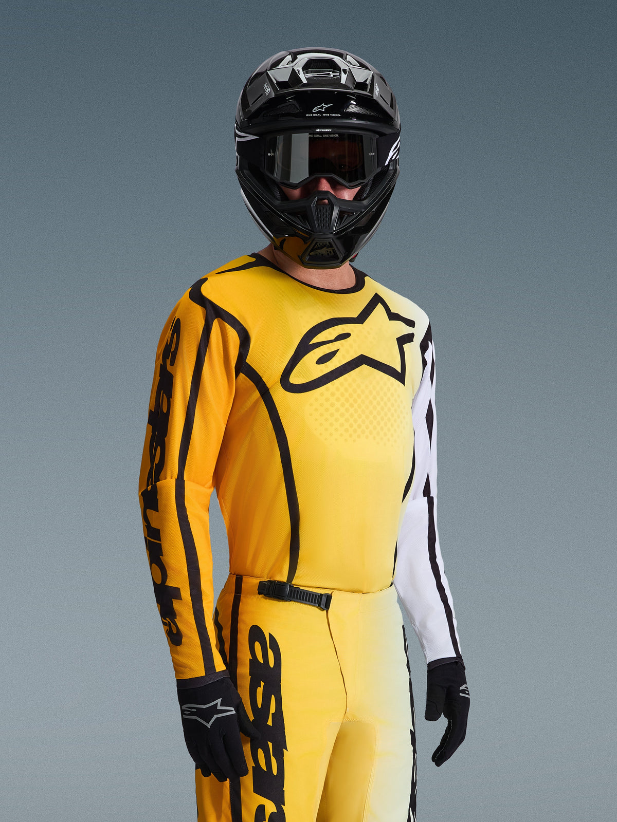 Maillot Alpinestars Fluid Apex 2026, maillot de motocross, jaune et noir avec des accents blancs, porté par un pilote avec un casque et des lunettes noirs, grand logo étoile noir sur la poitrine, tenue de course tout-terrain coordonnée