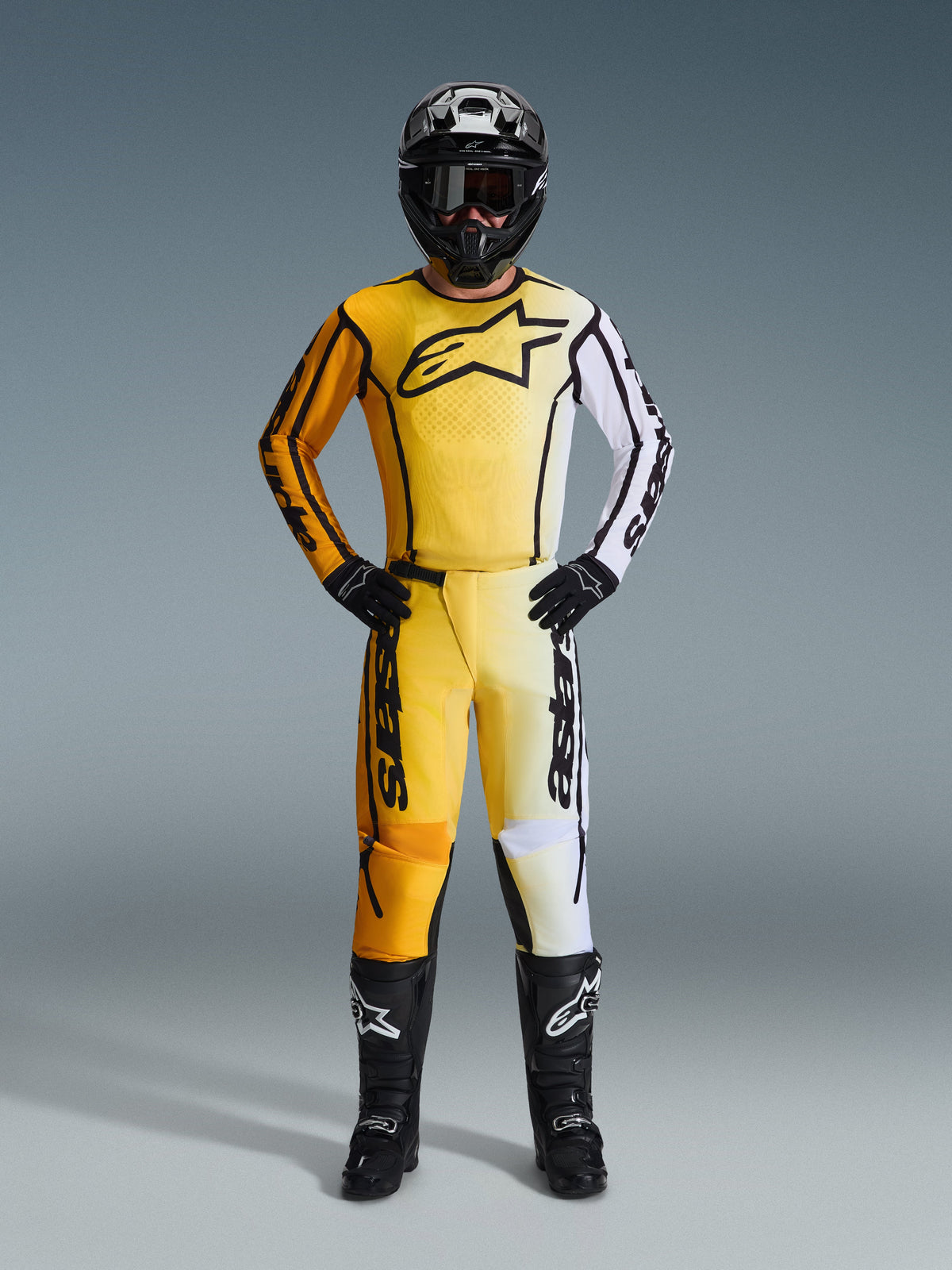 Pilote de motocross portant le maillot Alpinestars Fluid Apex 2026 en jaune et noir, pantalon assorti avec des accents blancs, casque noir, gants noirs et bottes noires, équipement de course professionnel complet pour le motocross
