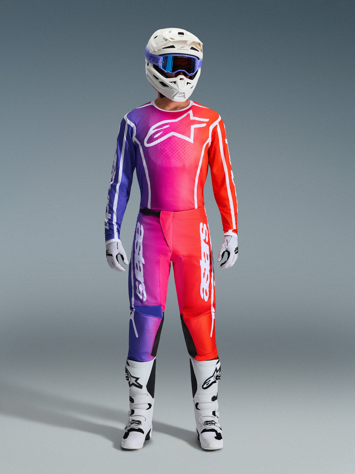 Équipement de motocross complet Alpinestars 2026 Fluid Apex, maillot et pantalon avec dégradé de violet, rose et orange, logo blanc sur la poitrine, casque blanc avec lunettes bleues et bottes blanches, conçu pour la performance tout-terrain