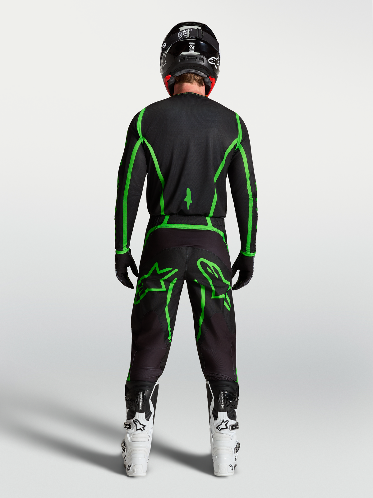 Alpinestars Pantalons Fluid Apex V2, pantalon de motocross noir et vert fluo, vue de dos sur un pilote avec bottes blanches.
