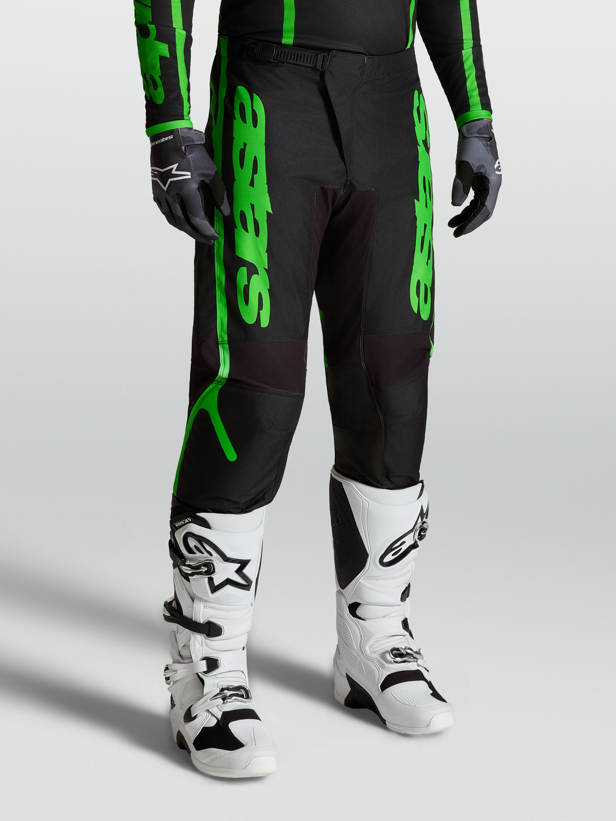 Alpinestars Pantalons Fluid Apex V2, équipement de motocross performance pour homme, noirs et vert fluo avec poly-tissu 600D renforcé, portés avec bottes et gants sur modèle