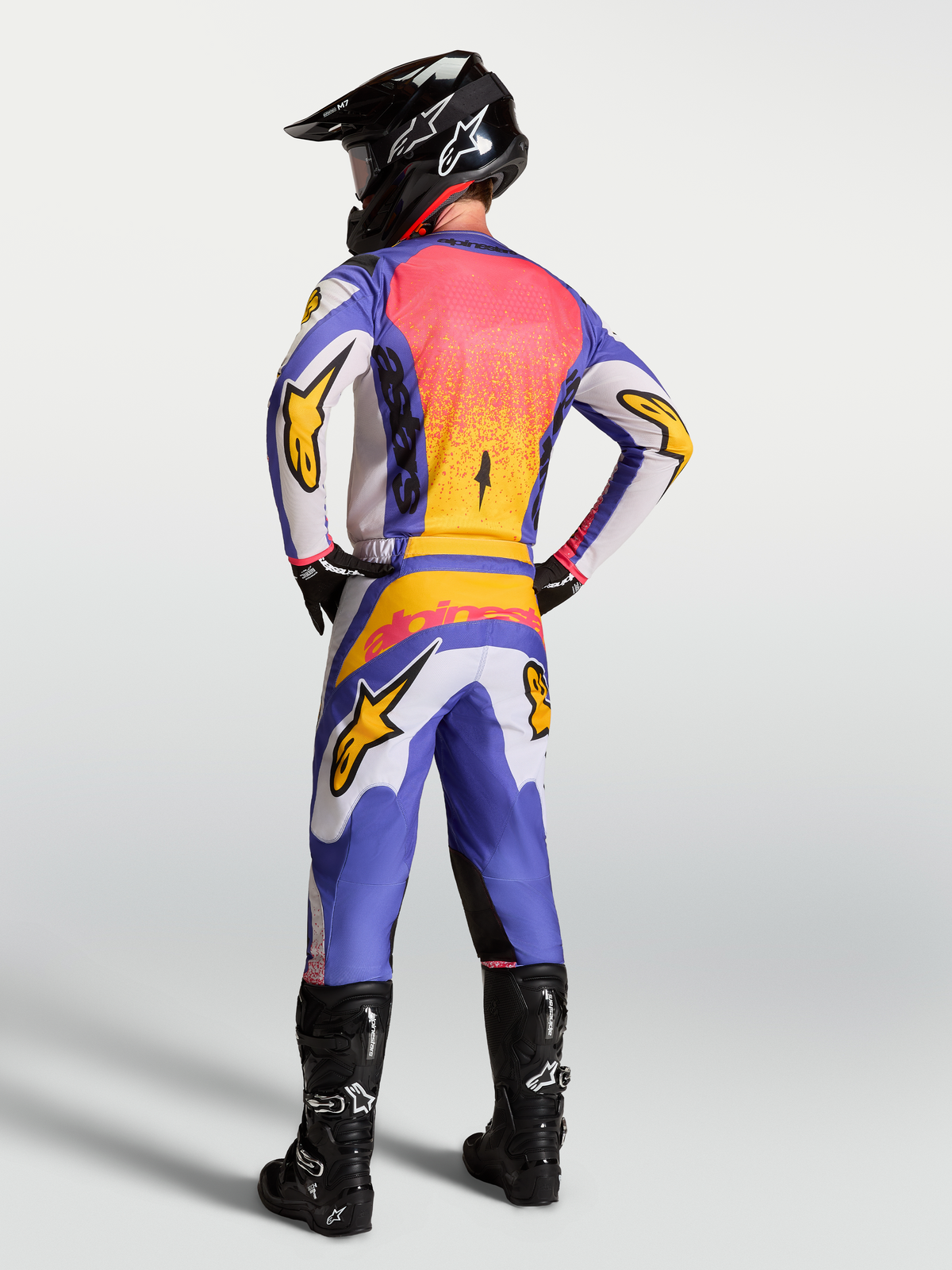 Maillot Alpinestars Fluid Drag, maillot de motocross lilas et bleu avec accents dorés, vu de dos sur un pilote.