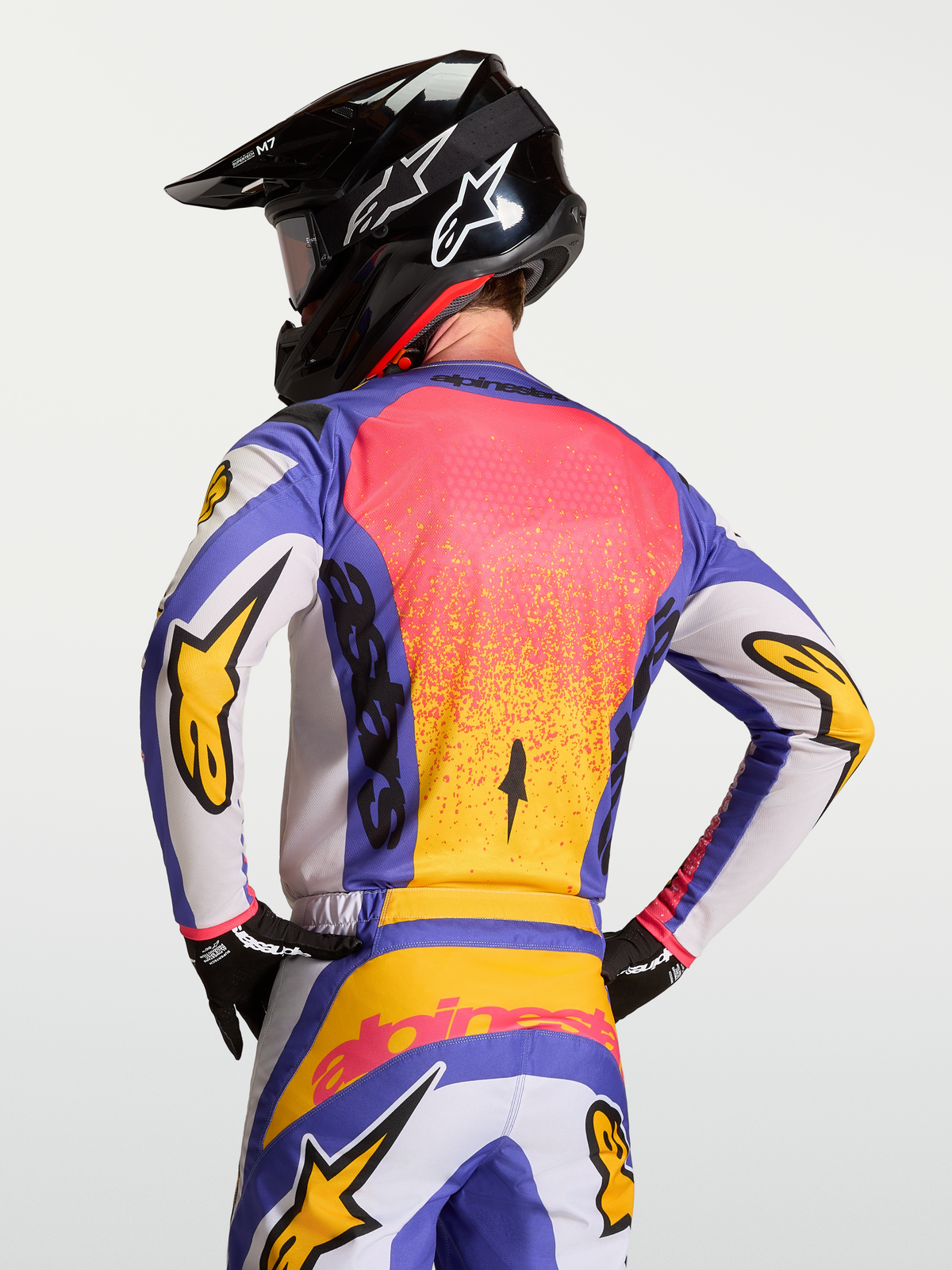 Maillot Fluid Drag Alpinestars, maillot de motocross bleu iris et doré, porté par un mannequin avec casque, tissu respirant et coupe arrière ergonomique