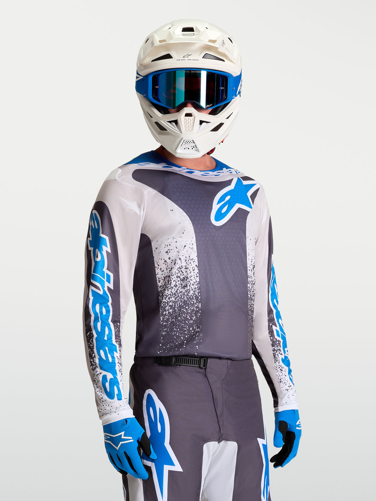 Alpinestars Fluid Drag Trikot, Performance-Motocross-Trikot in Grau und Blau, am Model mit weißem Helm und Handschuhen, atmungsaktiv für MX und Offroad.