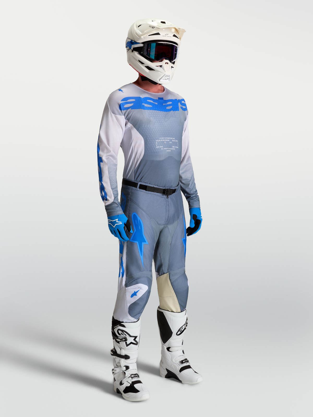 Alpinestars Racer Amber jersey, heren motorcrossuitrusting in grijs en blauw, model met helm en professionele motorlaarzen.