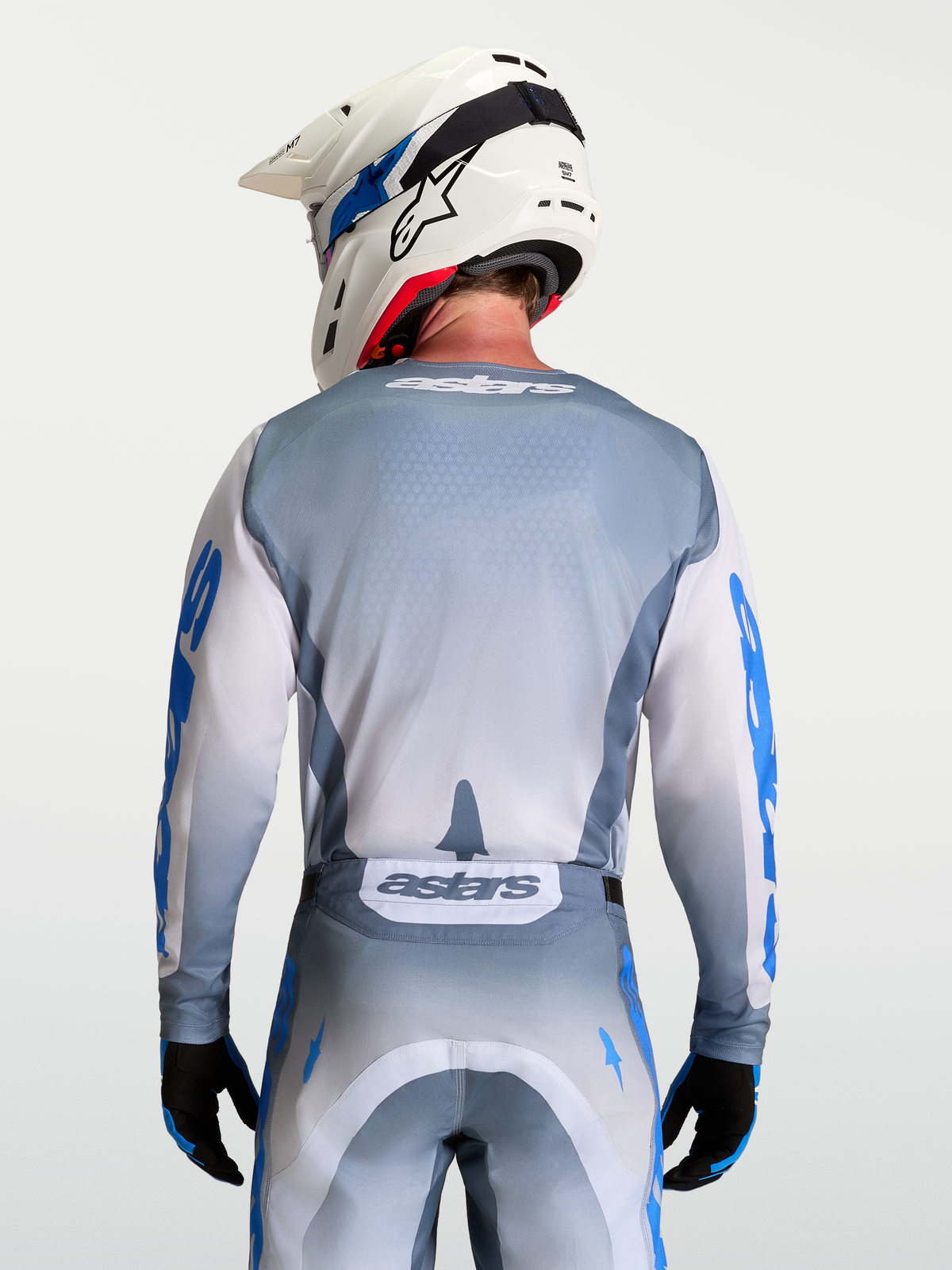Alpinestars Racer Amber Jersey, grijze en witte motocross jersey voor heren, ergonomische race-pasvorm, achteraanzicht op model met witte helm.