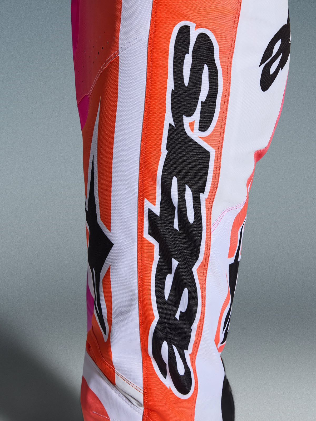 Alpinestars 2026 Racer Air Portl Hose, Motocross-Hose, Weiß, Orange und Pink, Nahaufnahme des Beins mit vertikalem schwarzem Alpinestars-Branding auf einem orangen Streifen, großem schwarzem Astars-Logo und atmungsaktivem, perforiertem Gewebe.
