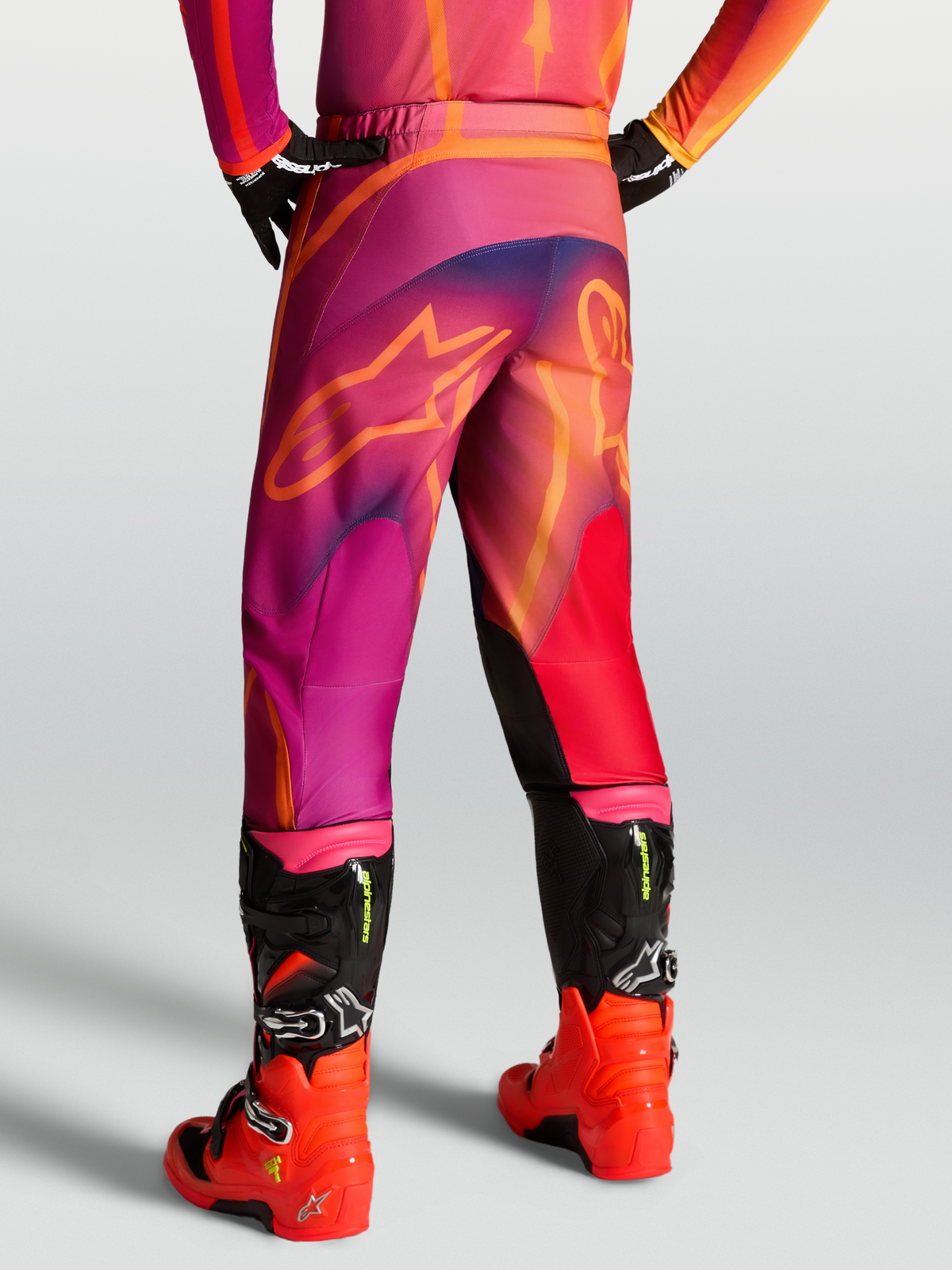 Alpinestars Fluid Kepler, pantalon de motocross pour homme, violet et orange, vu de dos sur un pilote avec bottes assorties, design pré-courbé en poly-tissu 600D durable et inserts extensibles.