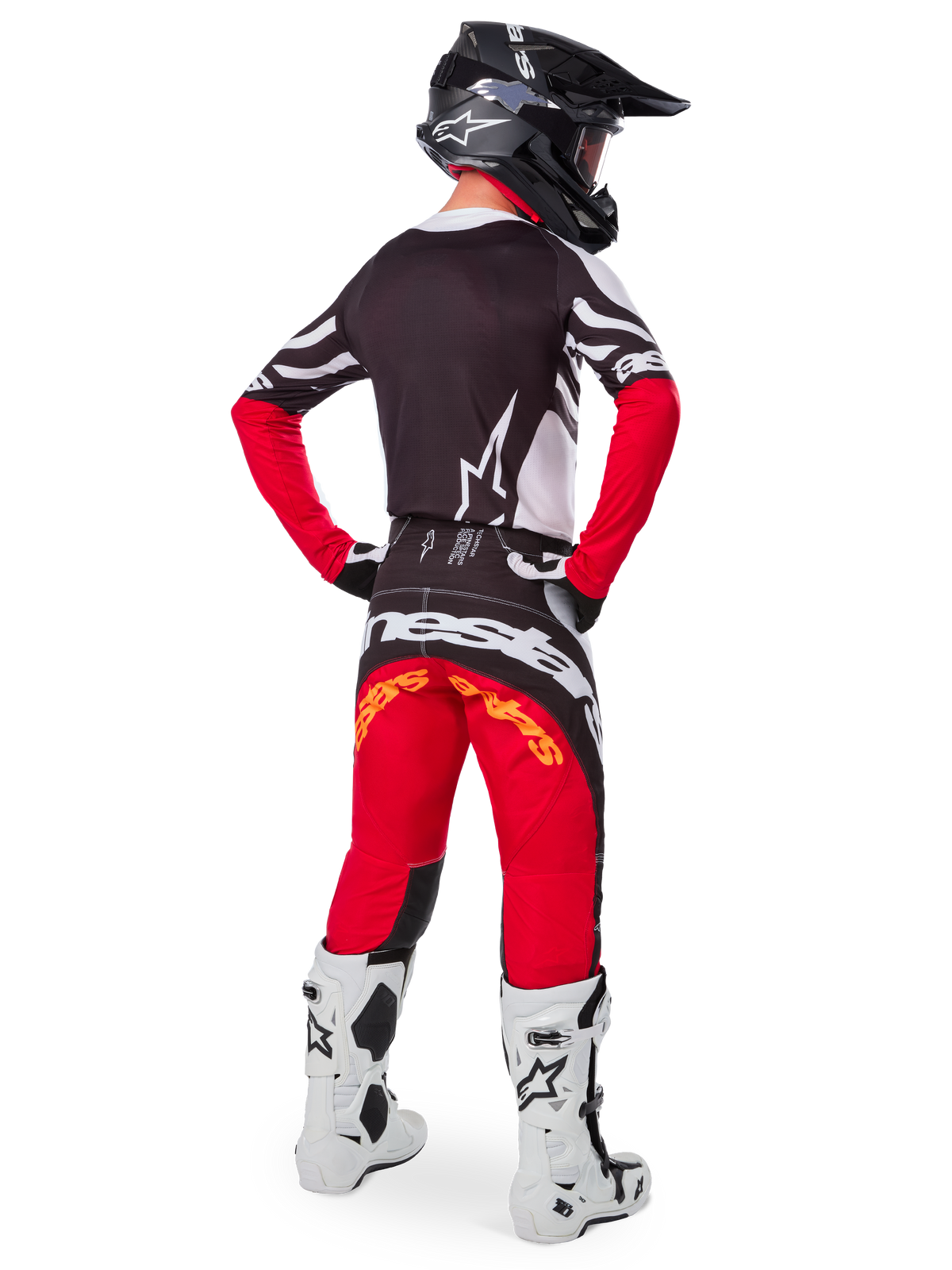 Vue arrière d'un pilote de motocross portant l'ensemble Techstar Deep Édition Limitée d'Alpinestars, comprenant un maillot noir avec des accents blancs et rouges, un pantalon rouge et noir assorti avec logo Alpinestars, des bottes de course blanches et un casque noir, présentant la tenue de course tout-terrain complète.